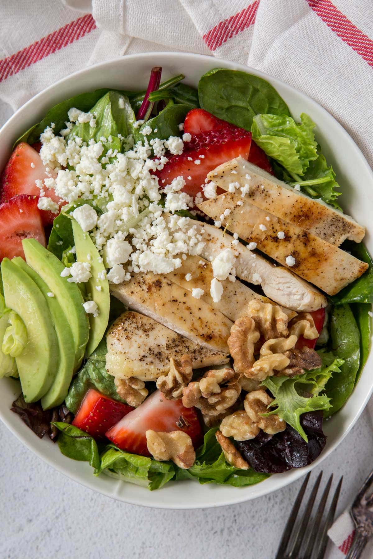 overhead of strawberry chicken salad with avocado, chicken, feta, lettuce, white bowl