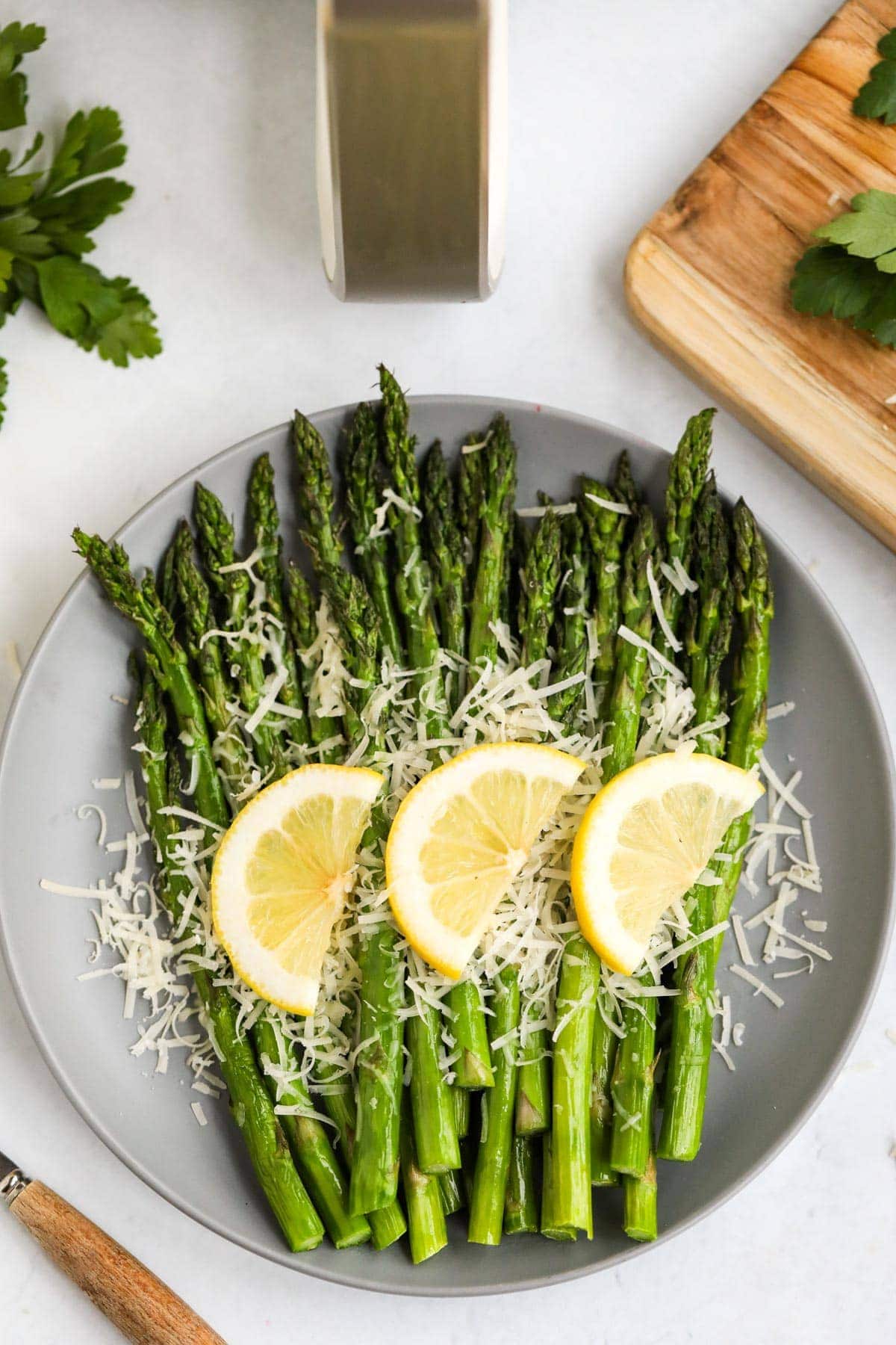 white plate, asparagus with lemon slices and parmesan, wood cutting board, air fryer handle