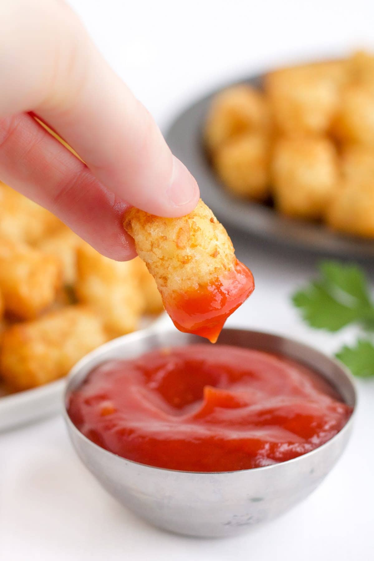 tater tots, ketchuup, tater tot dipped in ketchup, a hand