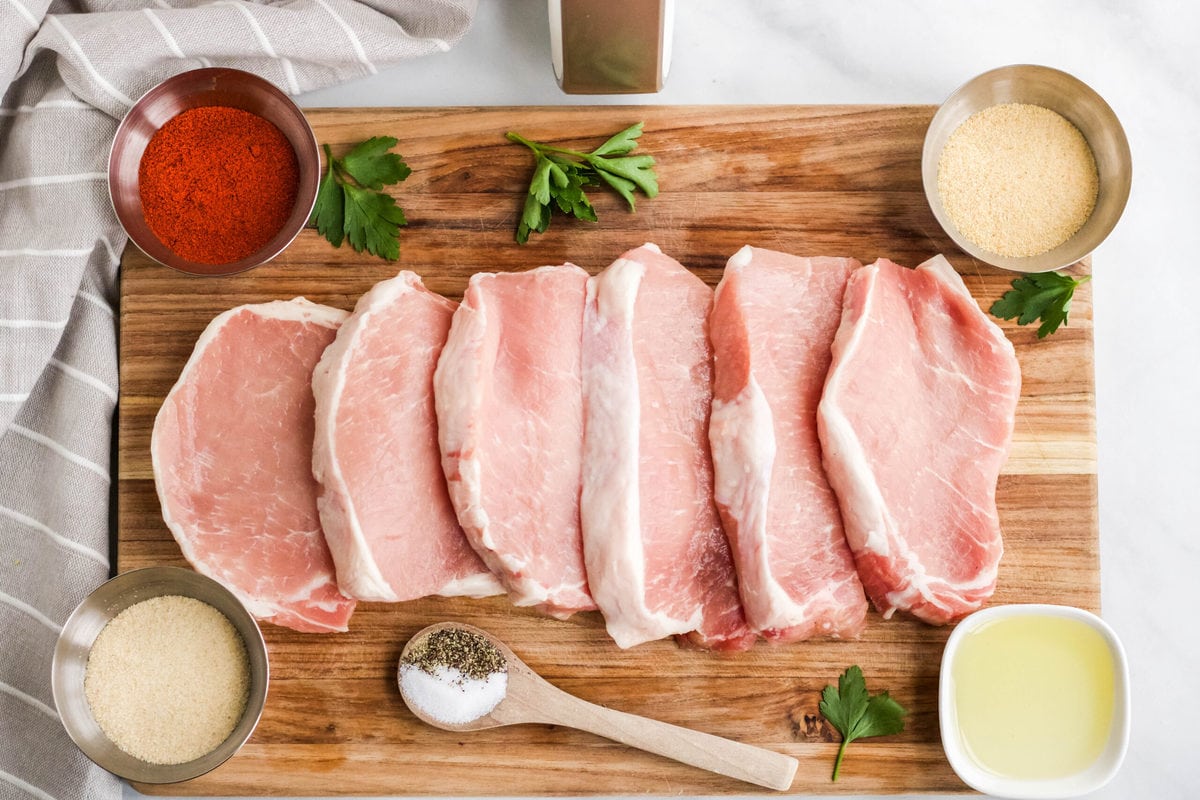 wood cutting board, raw pork chops, paprika, garlic powder, onion powder, olive oil