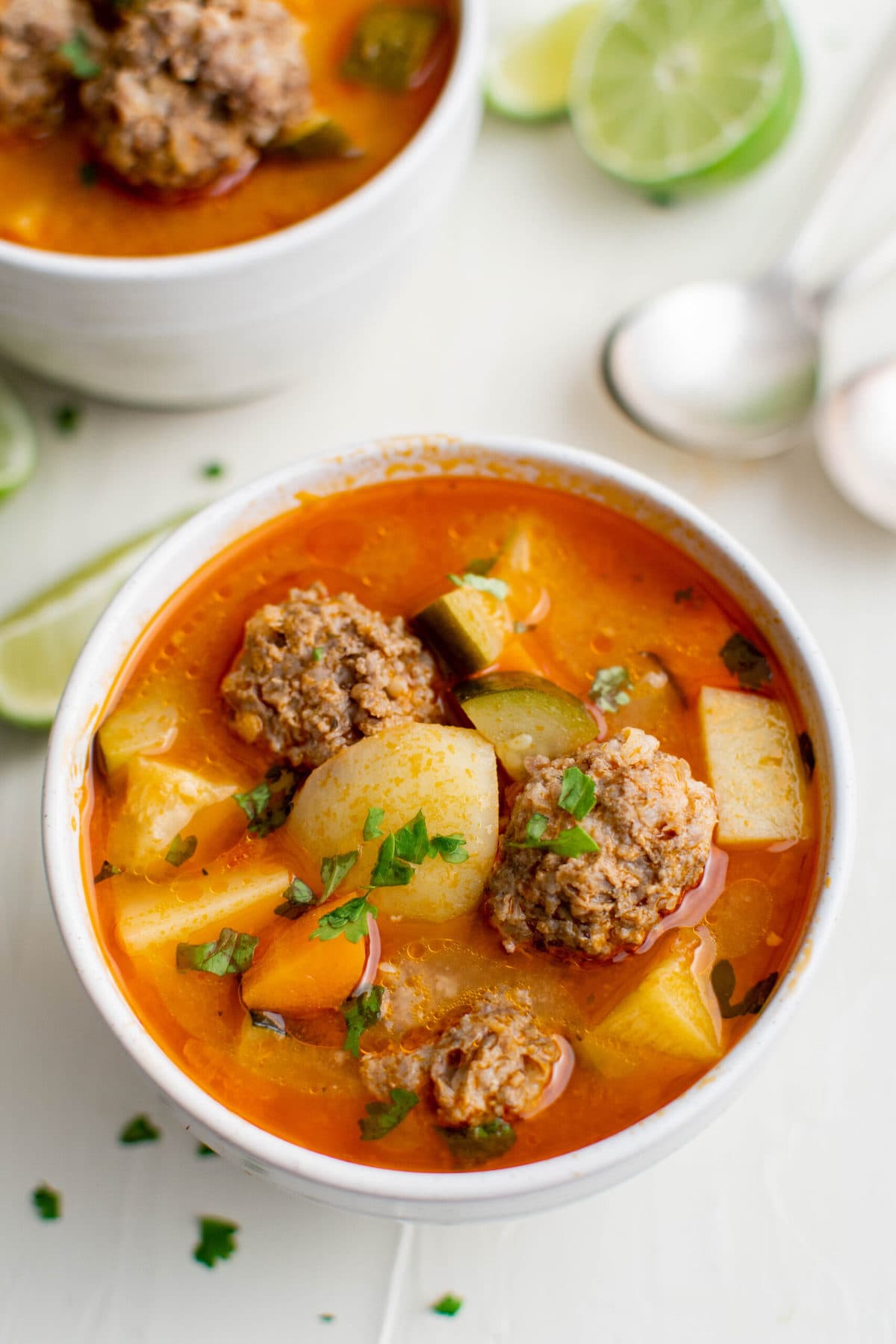 bowl of albondigas soup, spoons, limes