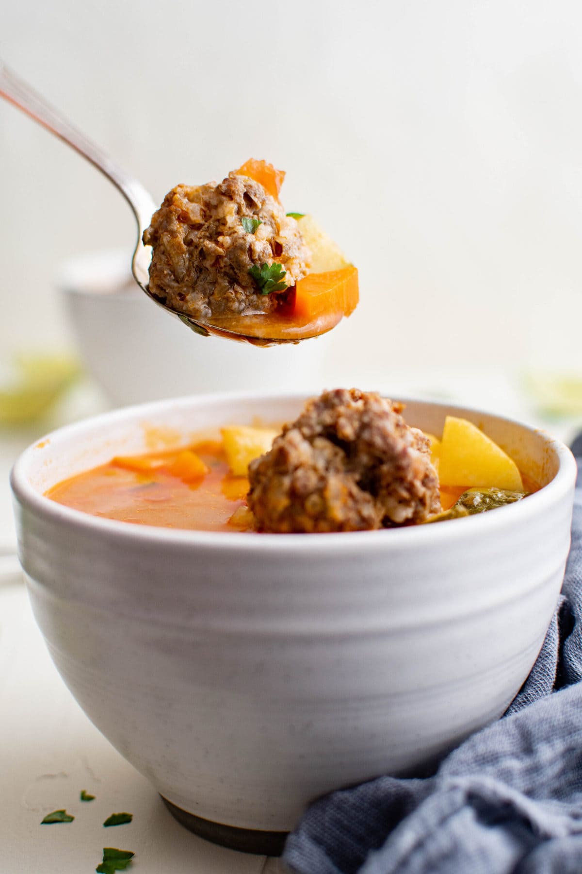 white bowl, spoon, meatballs, broth, blue napkin