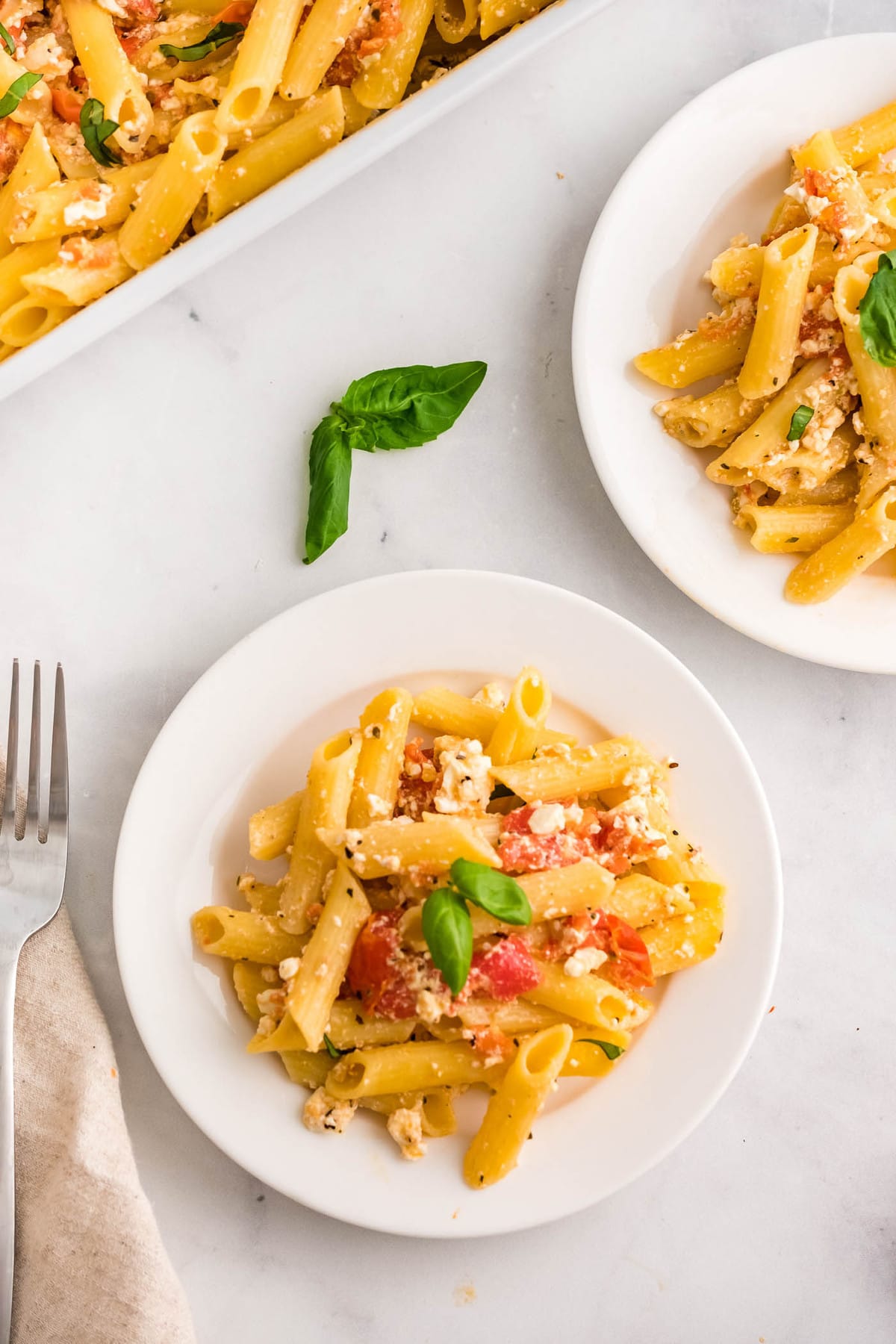 white plates, penne pasta, toamtoes, feta cheese, basil, fork