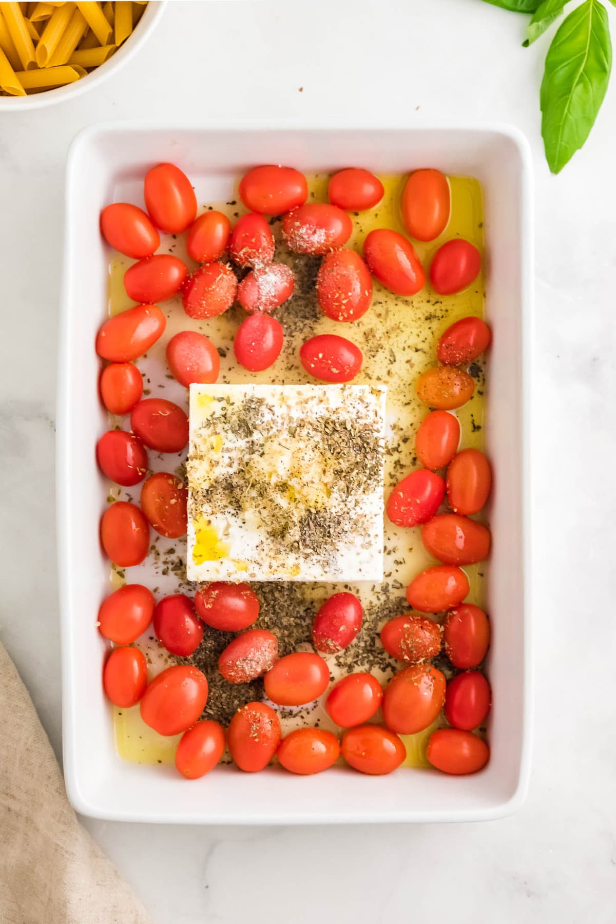 white baking dish, tomatoes, olive oil, block of feta, italian seasonings, pasta, basil