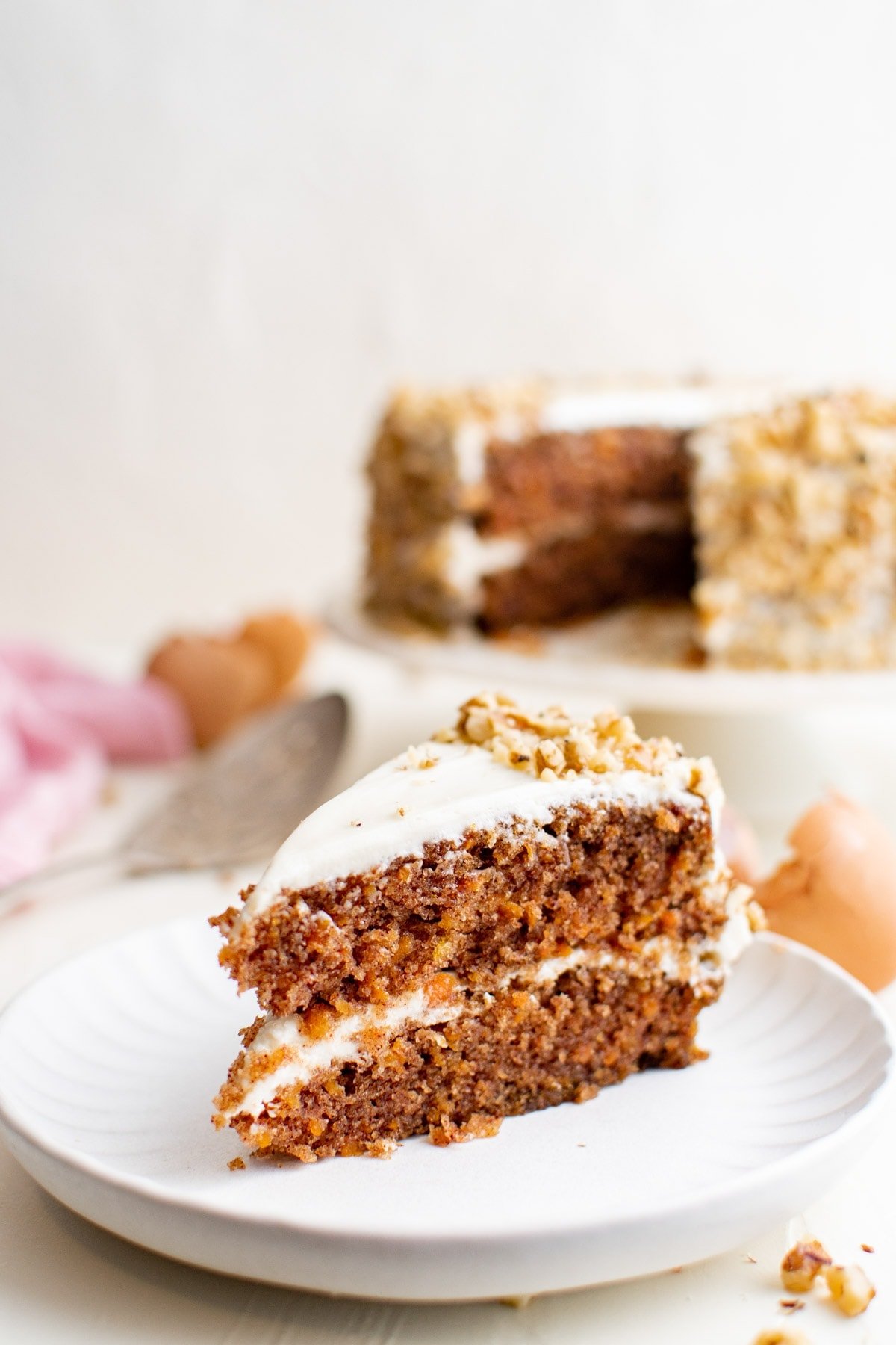 slice of carrot cake on a white plate, whole cake in the background