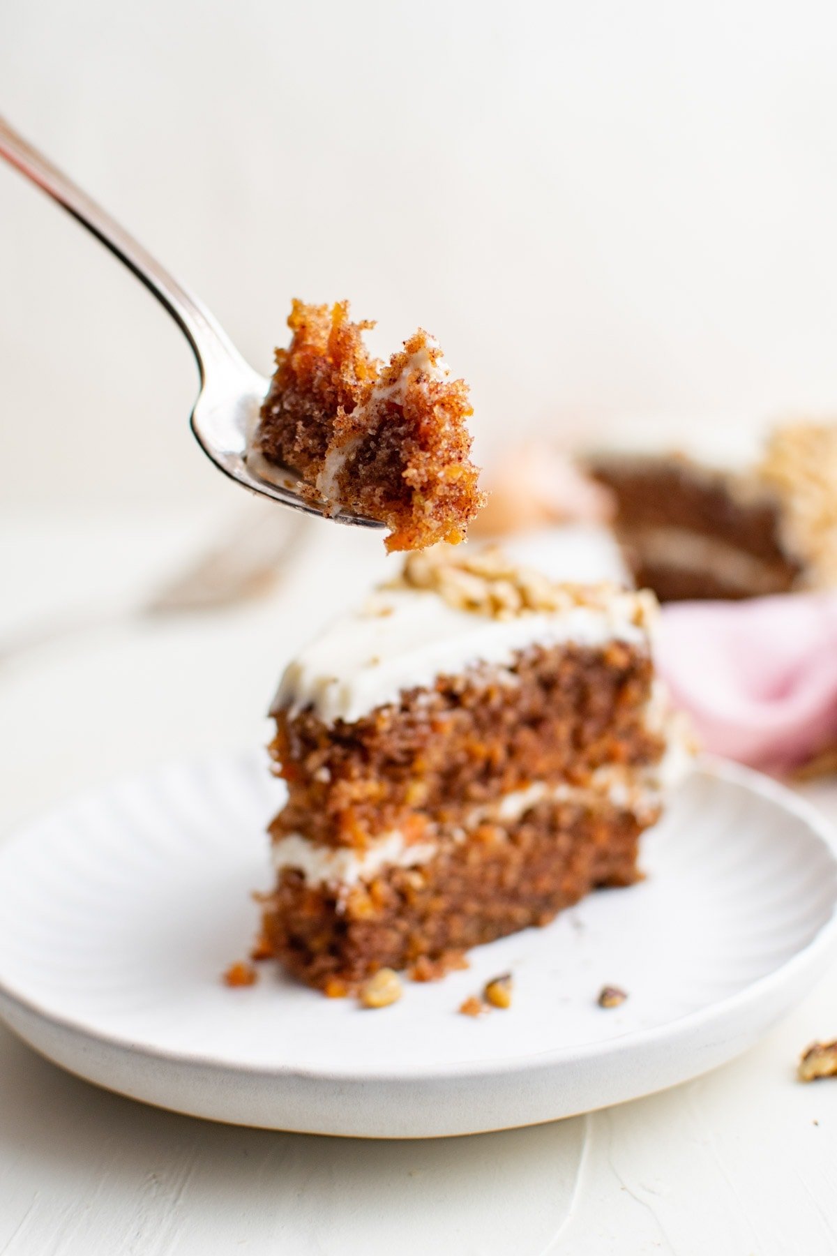 slice of carrot cake on white plate, fork, bite of cake