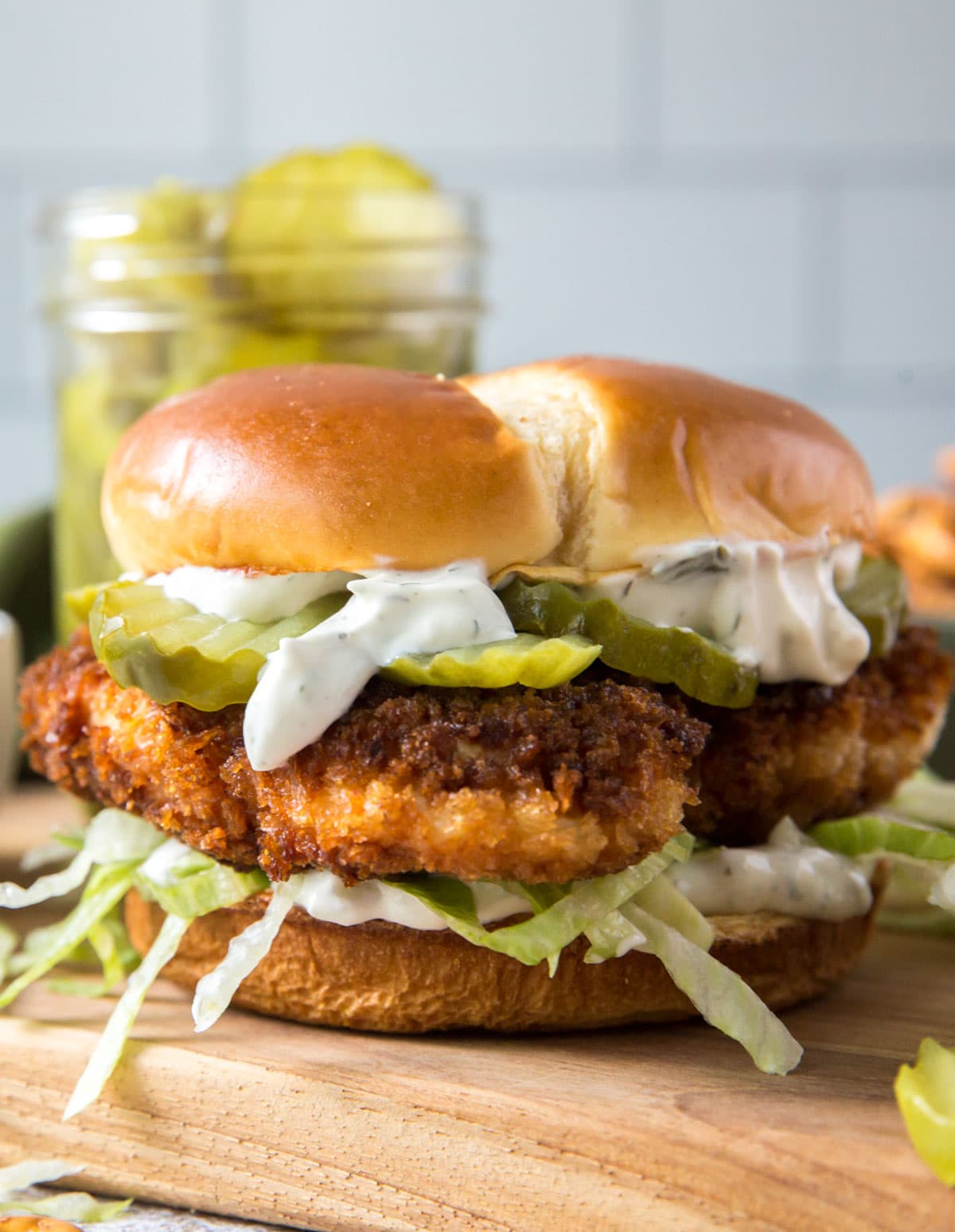 fried chicken sandwich with lettuce and pickles on a bin, wood cutting board, jar of pickles