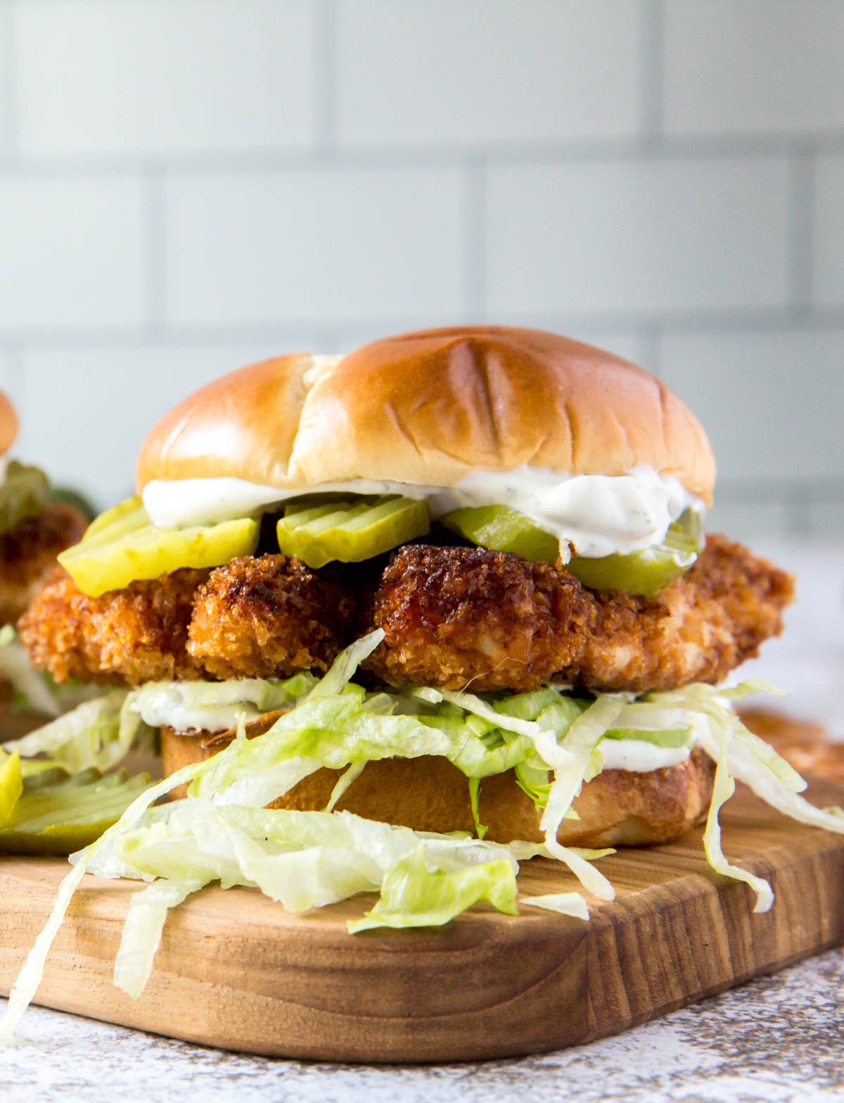 a crispy chicken sandwich with letttuce on a bun on top of a wood cutting board with pickles