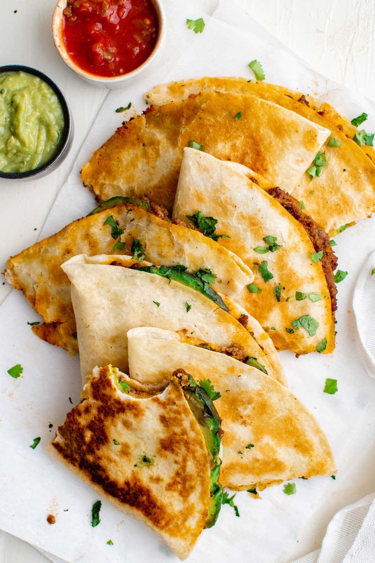 overhead shot of sliced ground beef quesadillas, guacamole, salsa