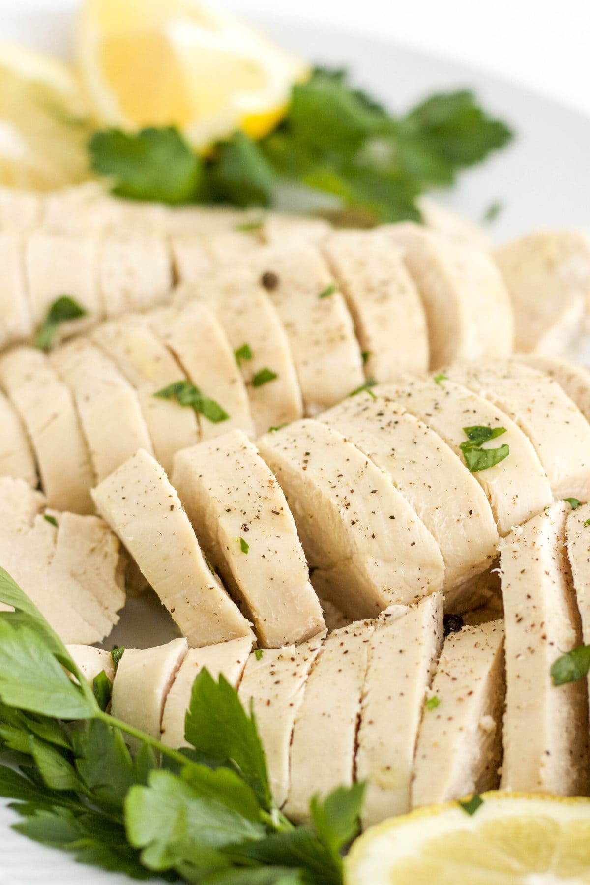 chicken breasts, sliced on a platter with parsley and lemon