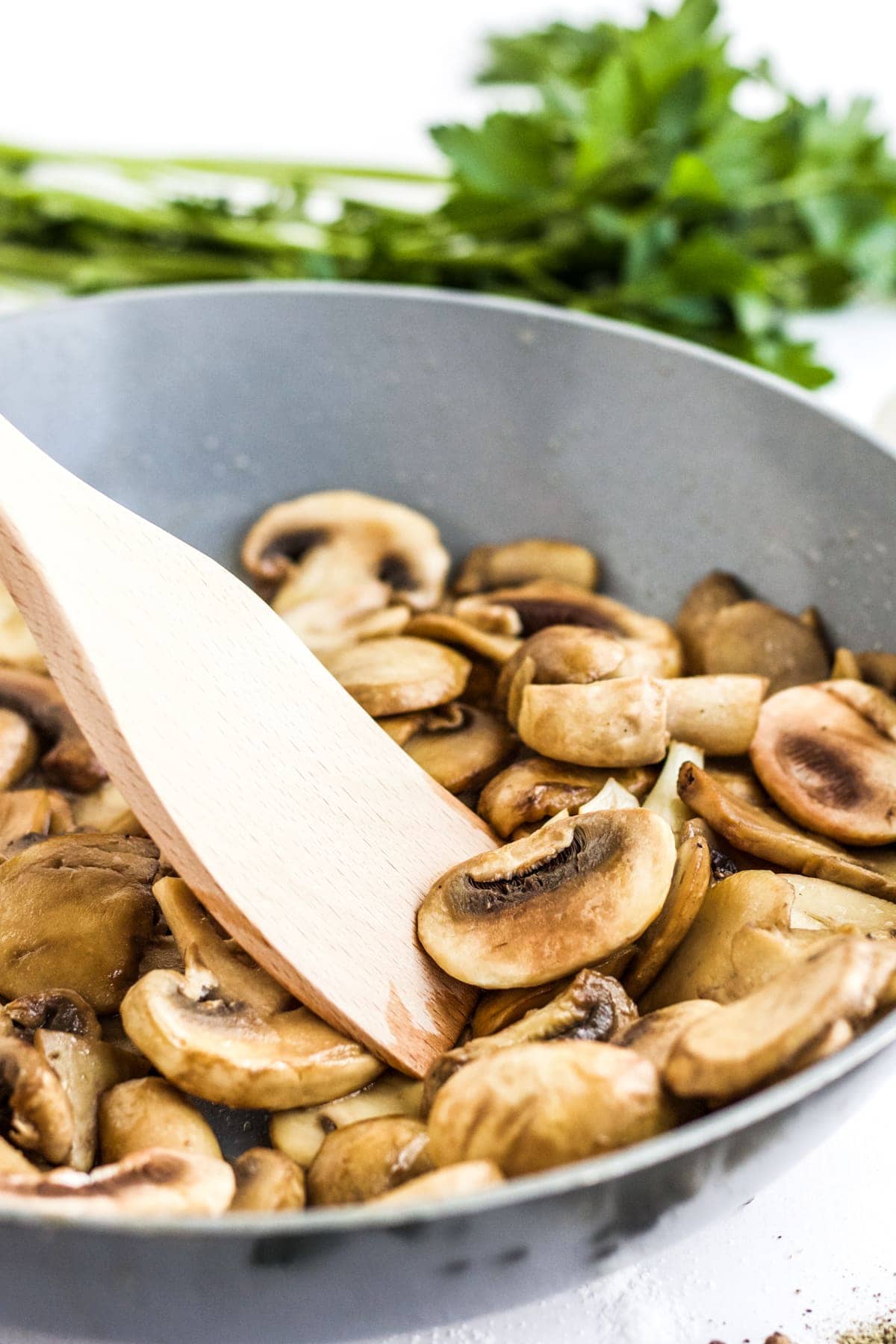Sauteed mushrooms in a frying pan with a wooden spatula moving them around. 