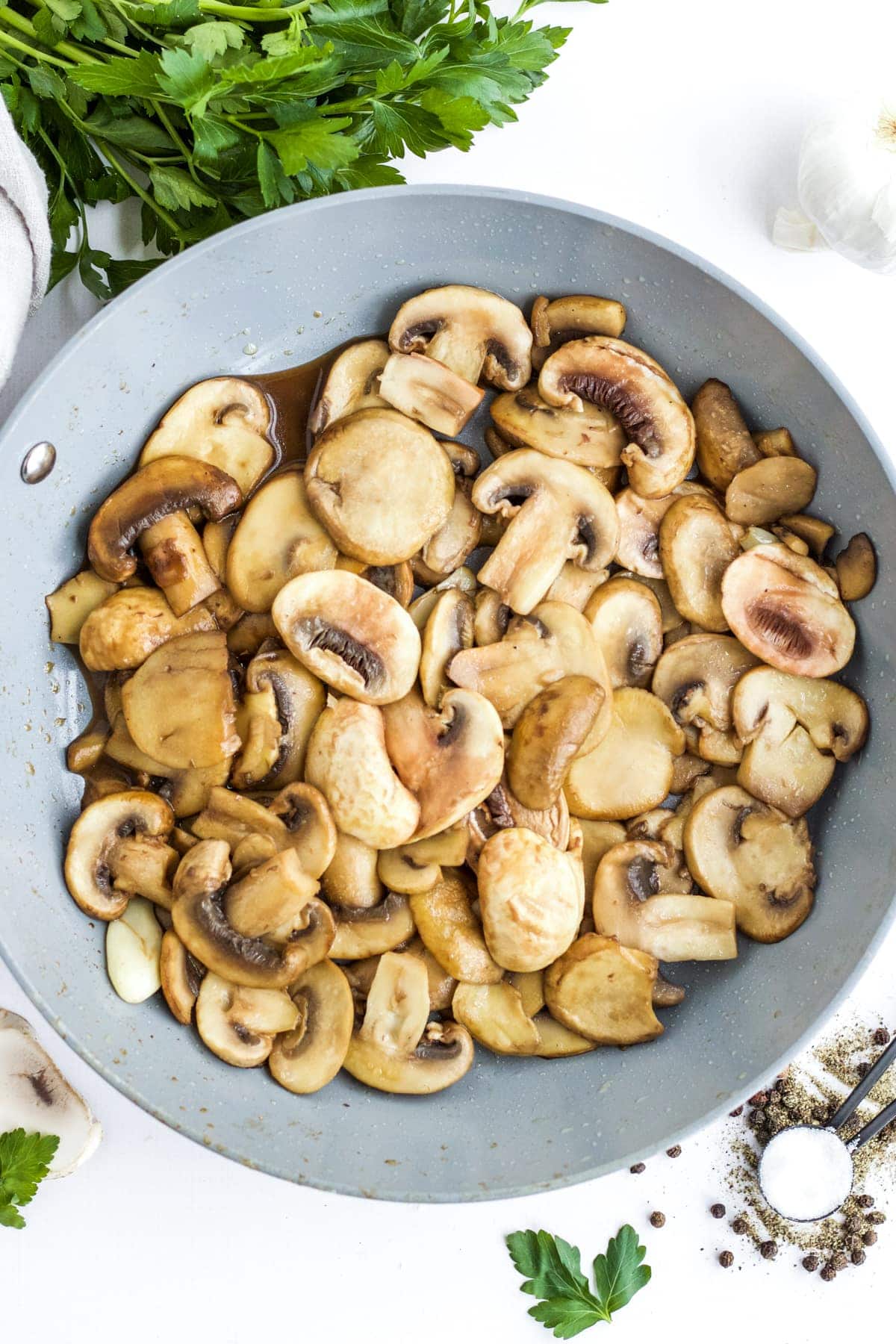 An overhead image of sauteed mushrooms in a skillet. Parsly, peppercors