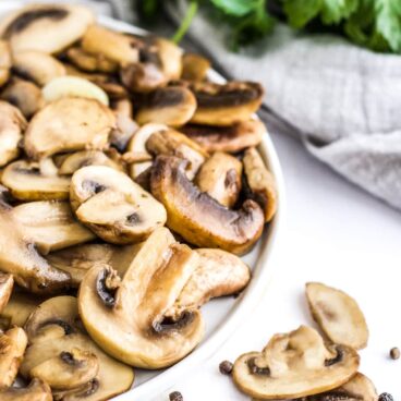 Sauteed Mushrooms on a white plate with herbs in the background.