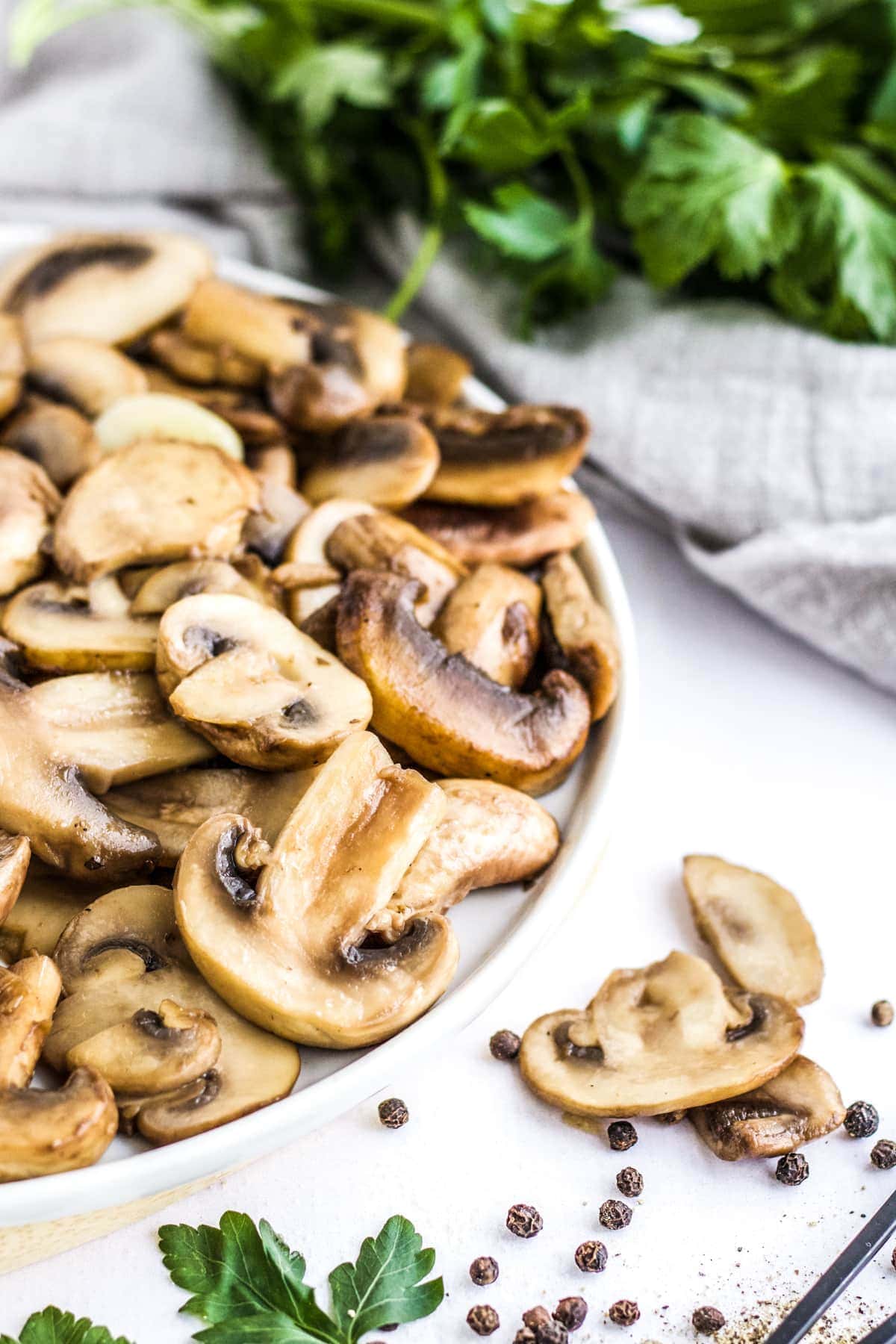 Sauteed Mushrooms on a white plate with herbs in the background. 