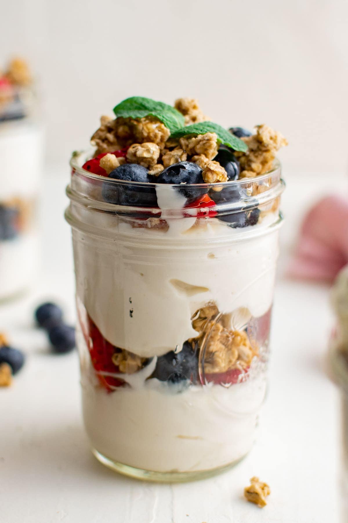 glass jar with yogurt, granola and berries and a mint sprig