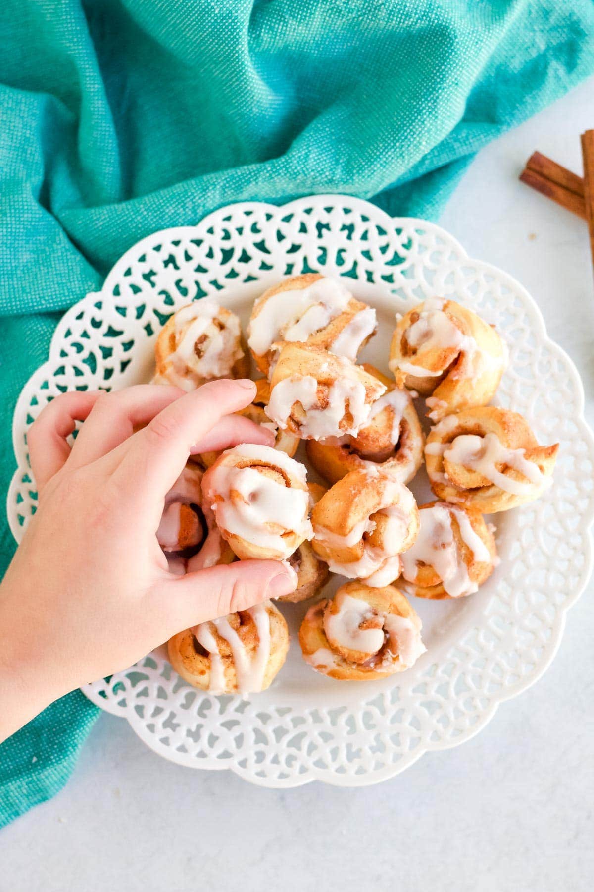 blue napkin, white lacy platter, hand reaching for mini cinnamon rolls