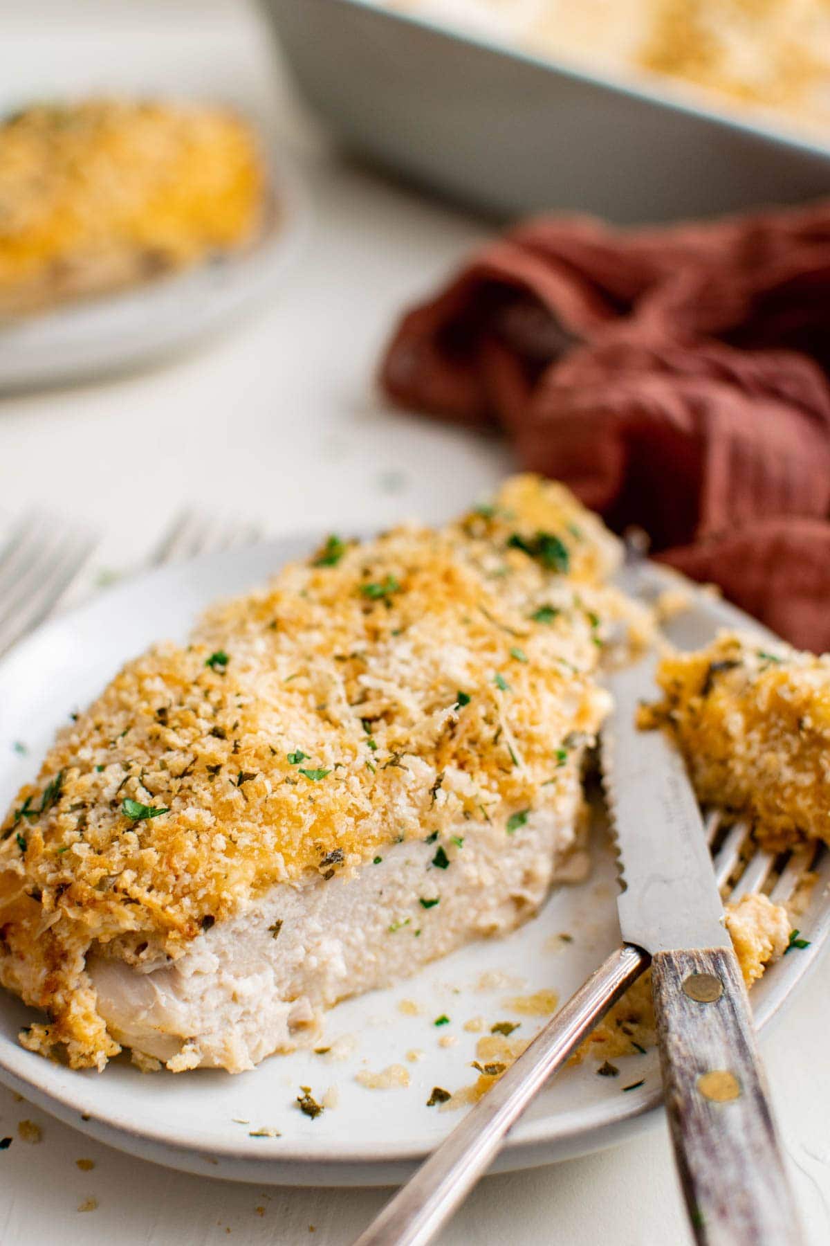 white plate, fork and knife, chicken breast cut with breadcrumbs on top