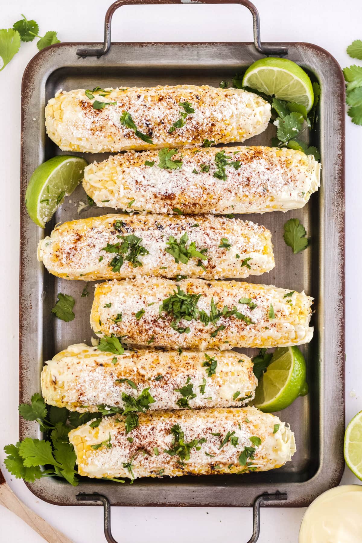 corn on the cob, mayo, cotija cheese, cilantro, limes on a silver tray