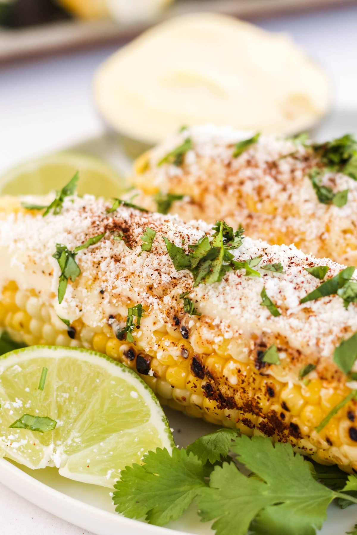 corn on the cob with cheese, cilantro and lime on a plate