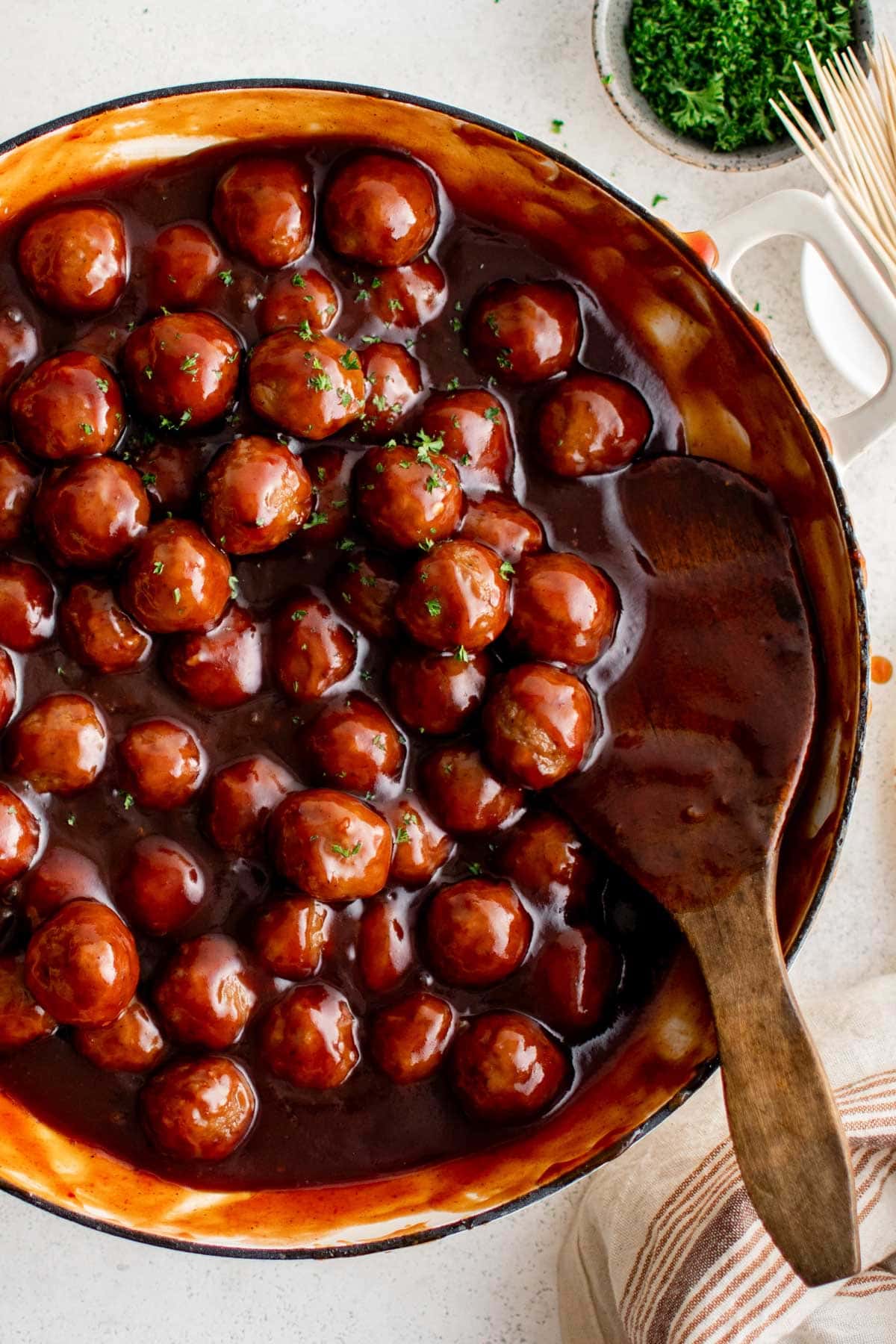 Spicy Barbecue Grape Jelly Meatballs | Game Day Appetizer | Party Food | Easy Dinner Recipe Meatballs in a dark red sauce with a wooden spoon.