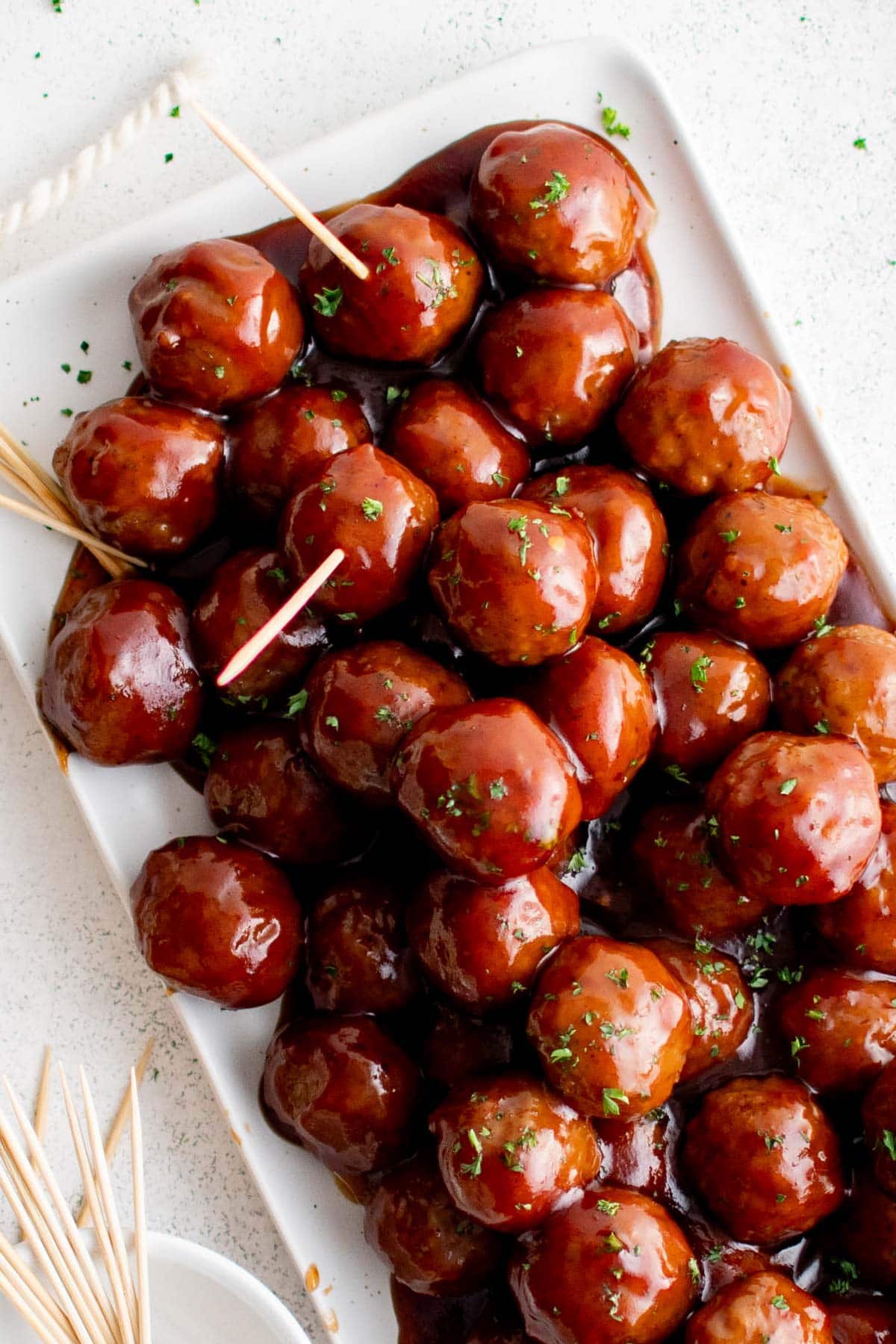 Spicy Barbecue Grape Jelly Meatballs | Game Day Appetizer | Party Food | Easy Dinner Recipe Grape Jelly Meatballs piled on a platter with a toothpick.