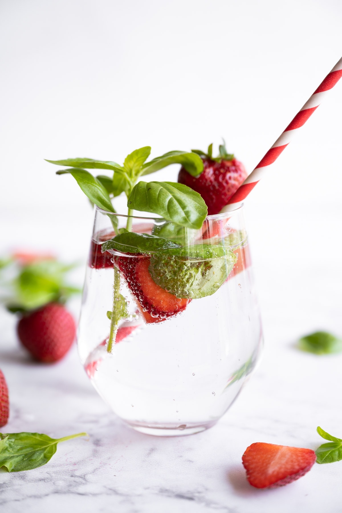 Strawberries and basil fruit infused water in a glass with a red striped straw.