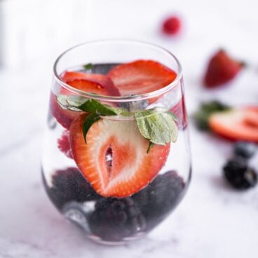 Strawberries, blueberries, and blackberries in a glass with water.