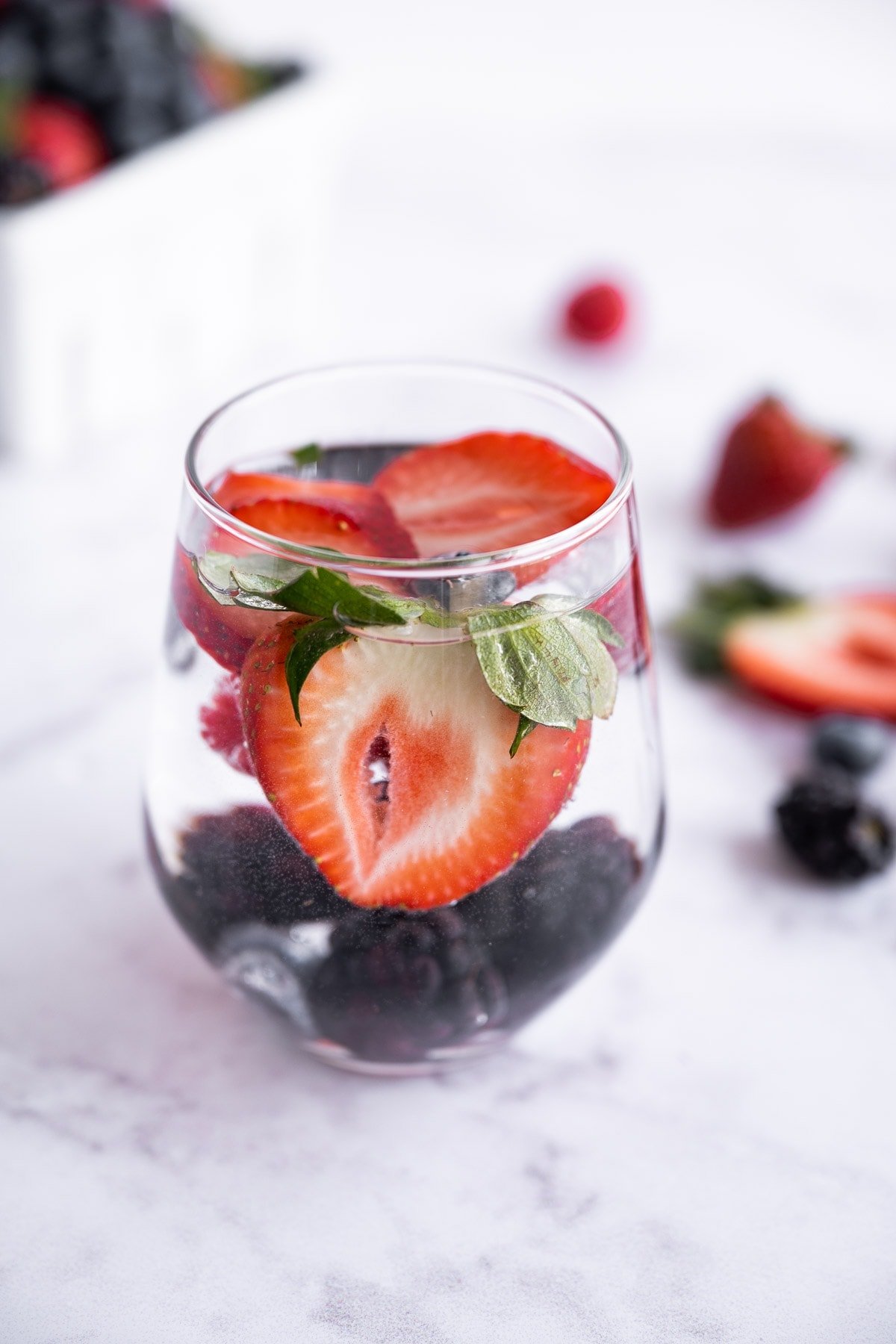 Strawberries, blueberries, and blackberries in a glass with water.