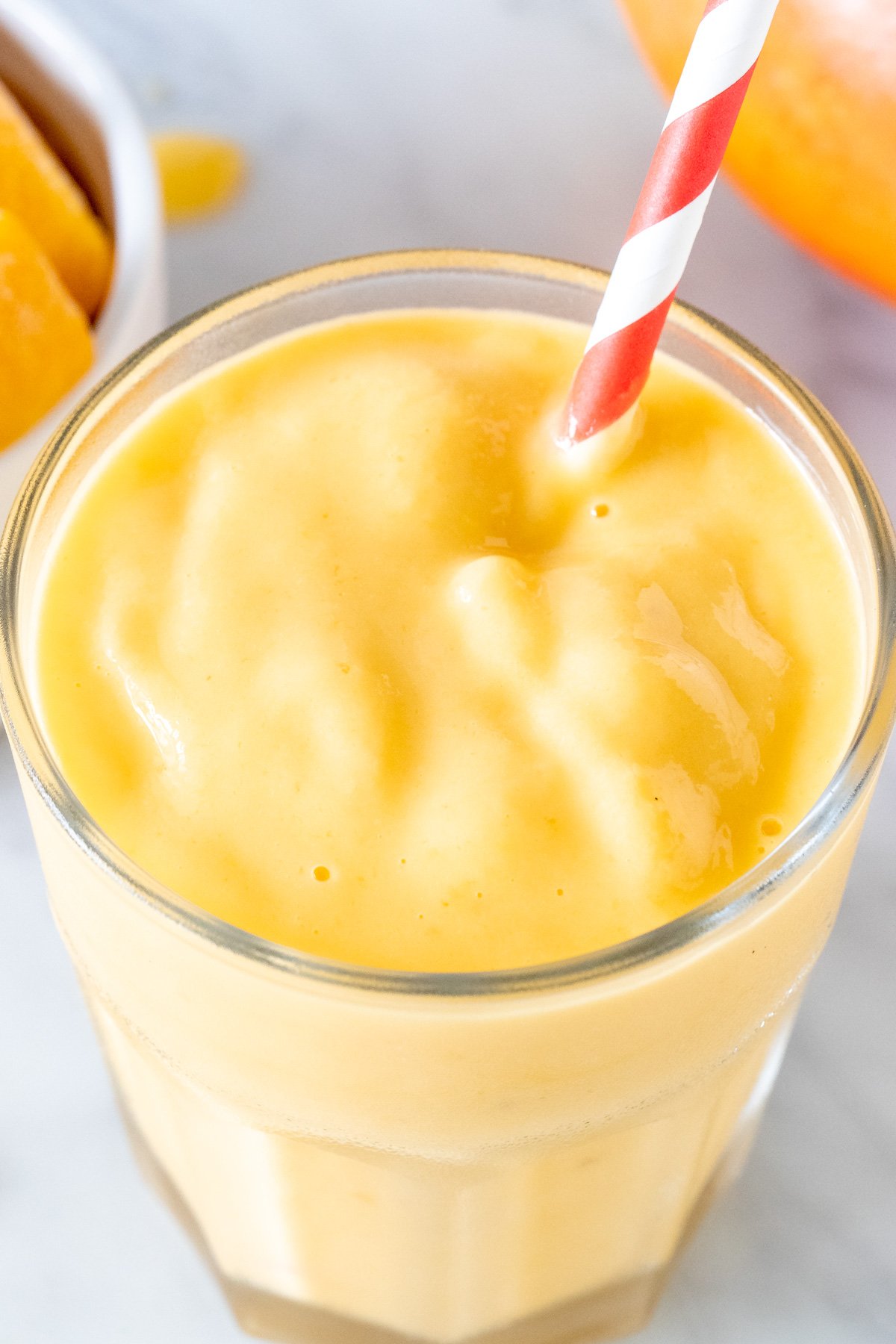 Thick mango smoothie in a glass, red and white straw, sliced mango fruit