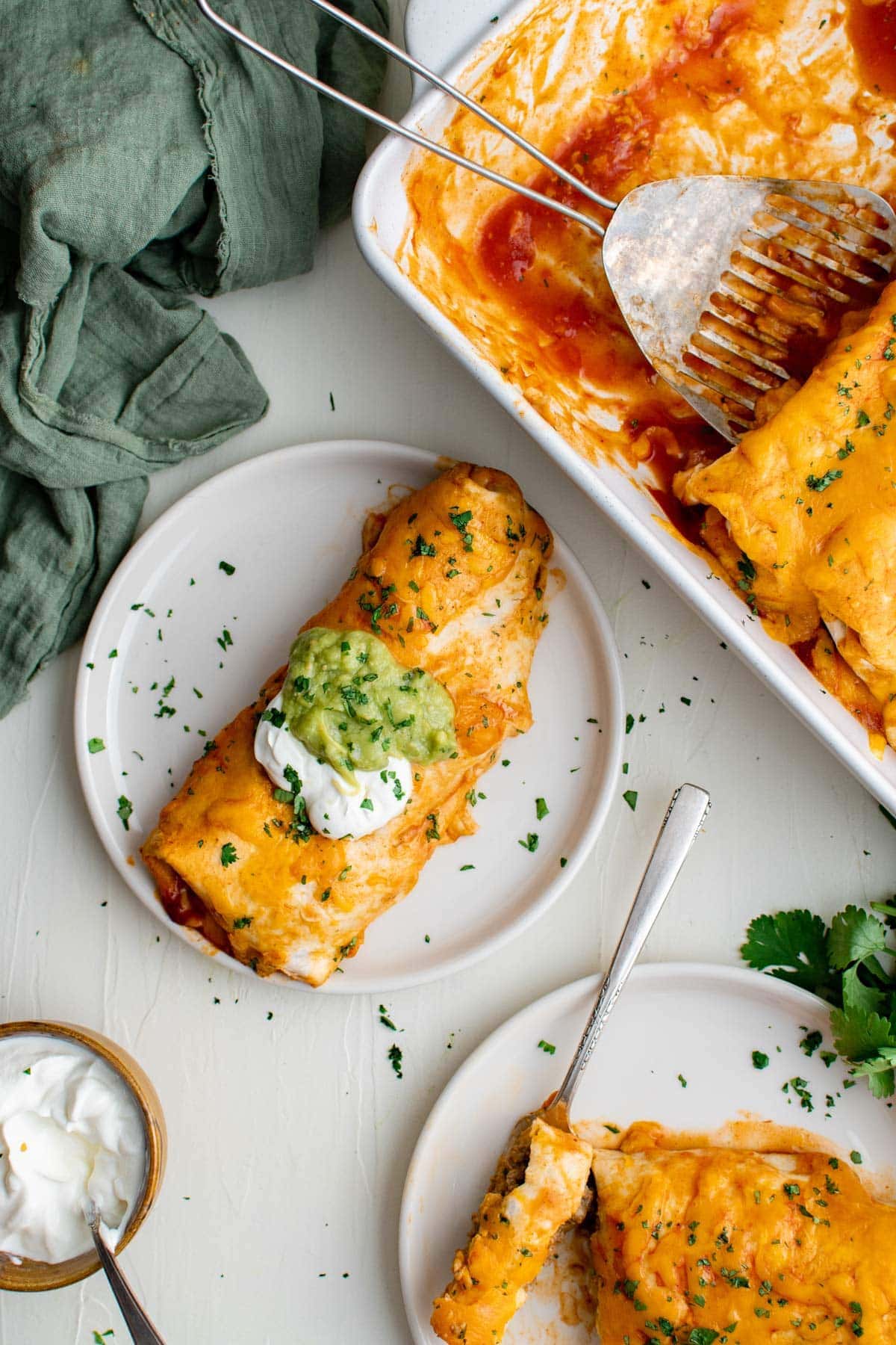 burrito topped with sour cream and guacamole on a white plate, surrounded by more burritos
