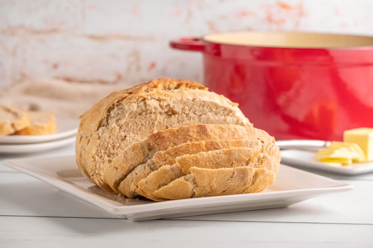 sliced sourdough bread on white plate, butter, red dutch oven