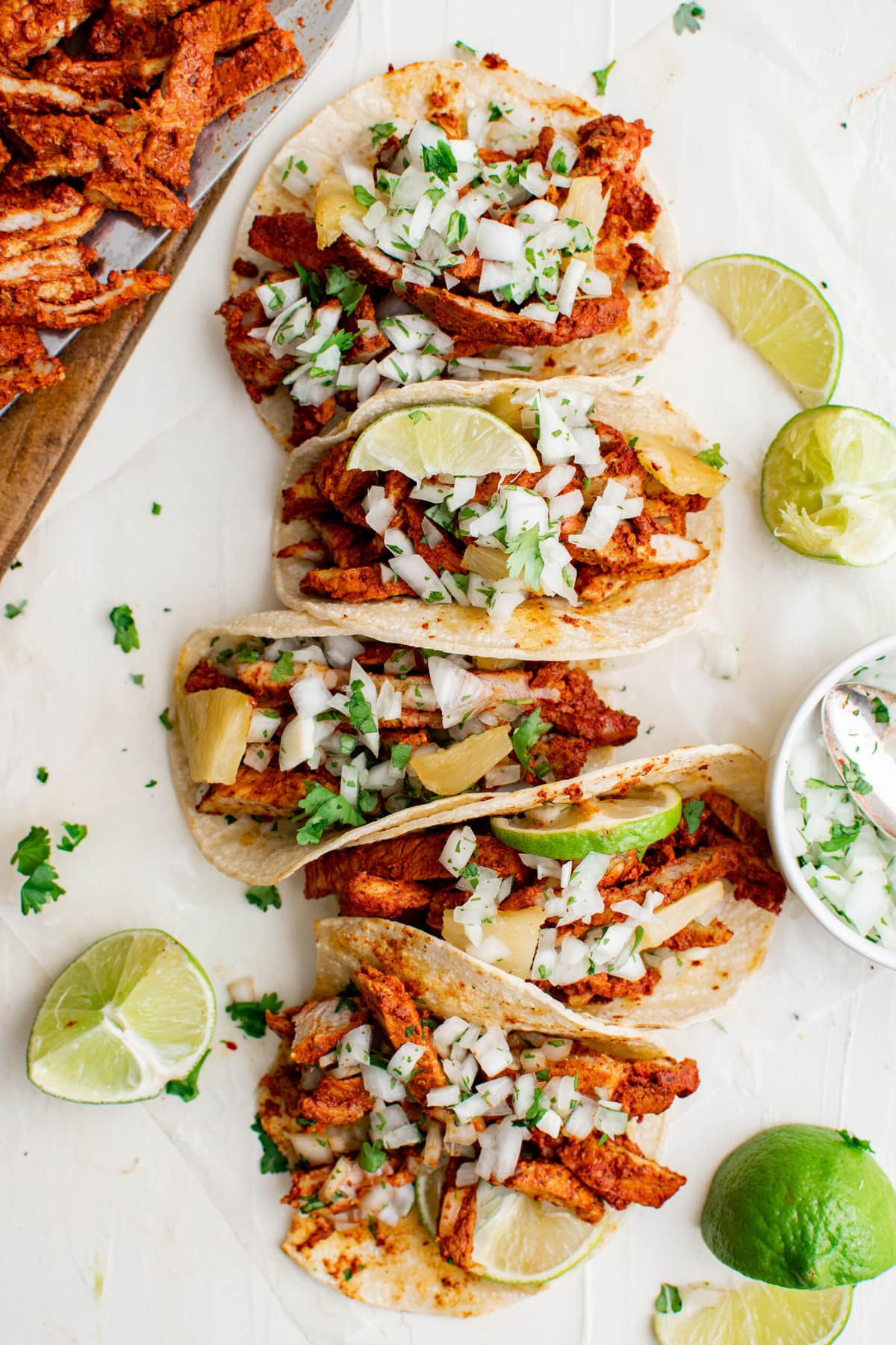 tacos al pastor lined up next to each other, limes