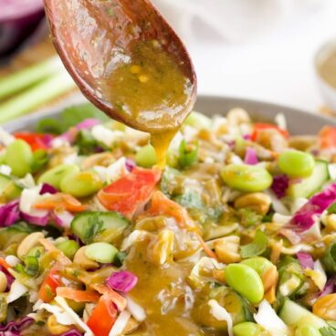 Thai Peanut Dressing being drizzles over a Thai Salad