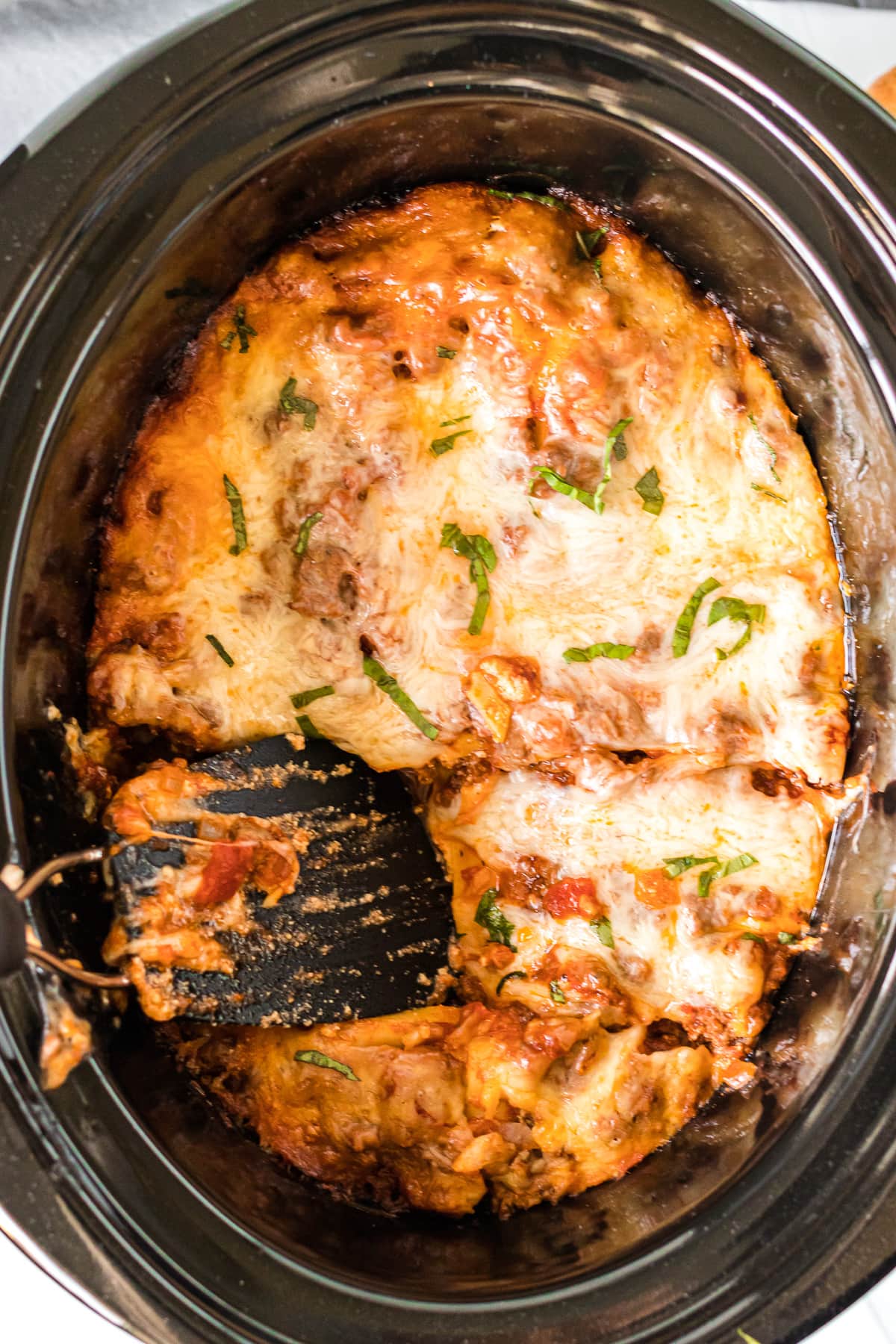 overhead shot of turner getting a portion of lasagna from the slow cooker