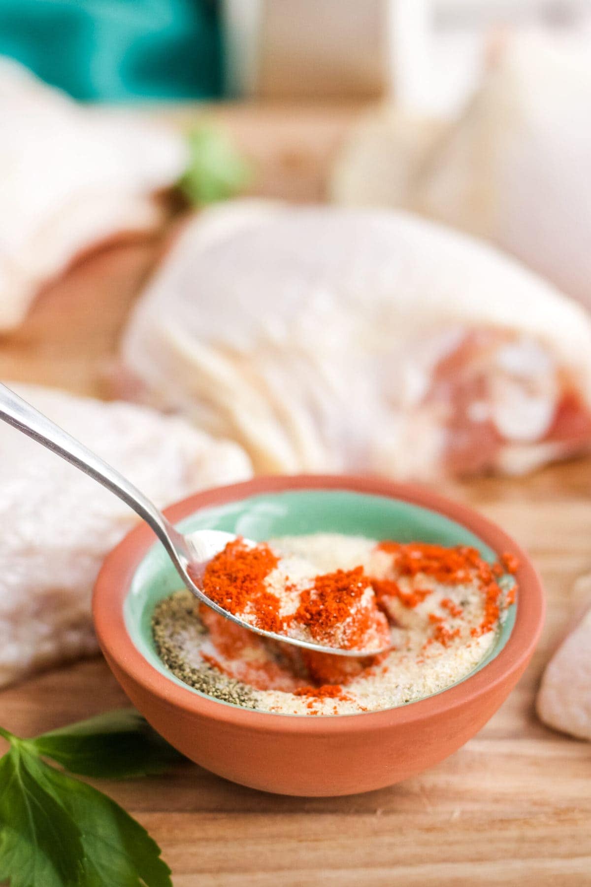 terracotta dish with chicken seasoning, spoon, raw chicken thighs