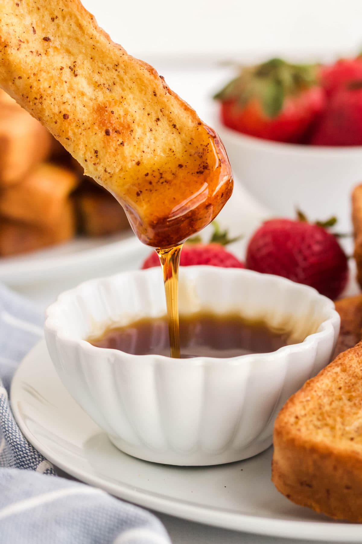french toast dipped in syrup, strawberries, white dishes