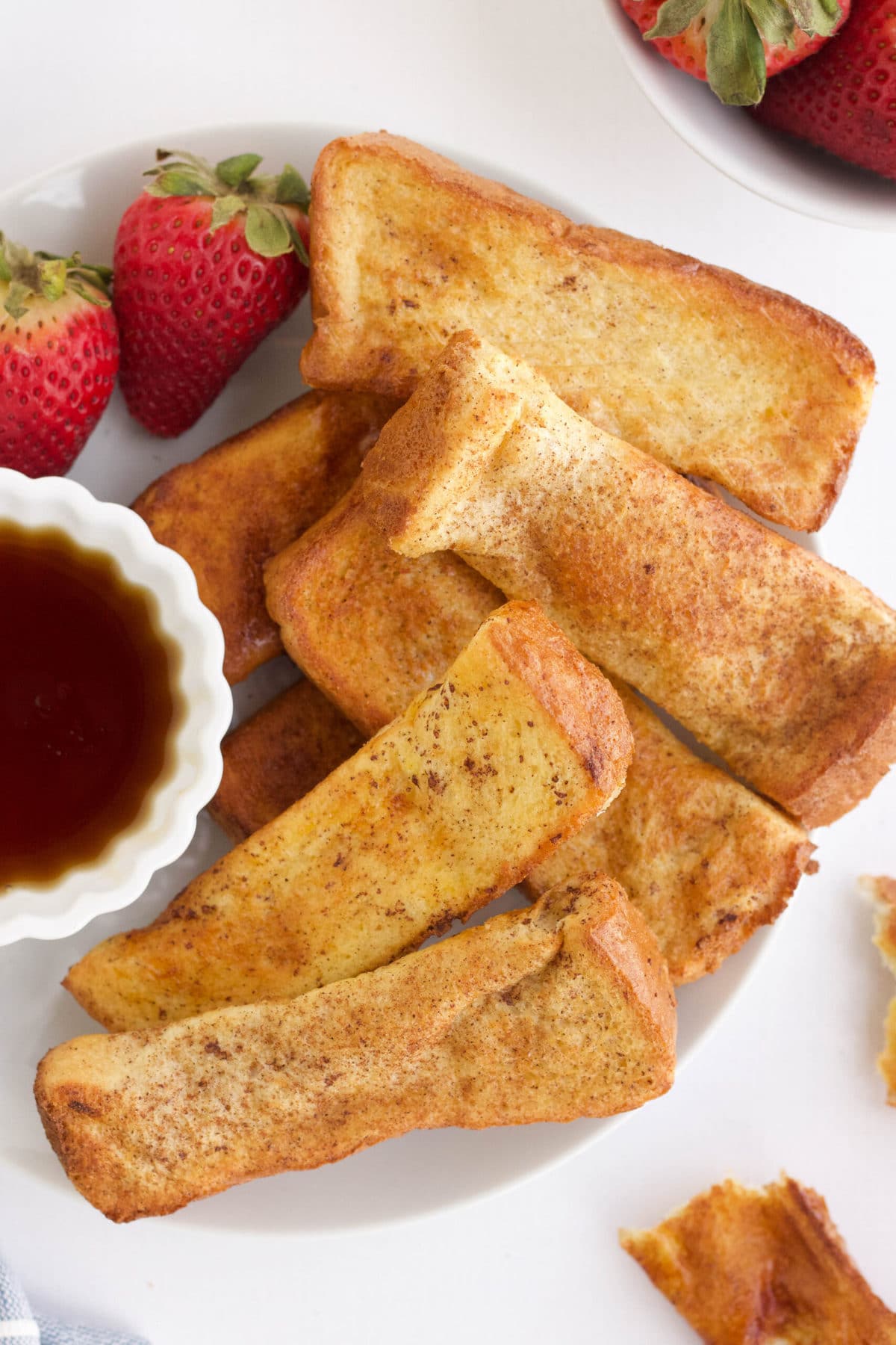 french toast on a white plate, small dish of syrup, strawberries