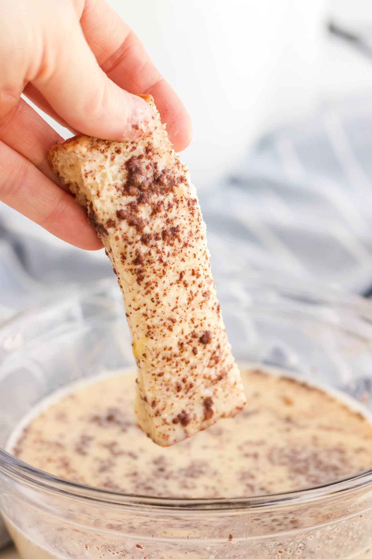 hand holding slice of bread dipped in egg, milk cinnamon mixture