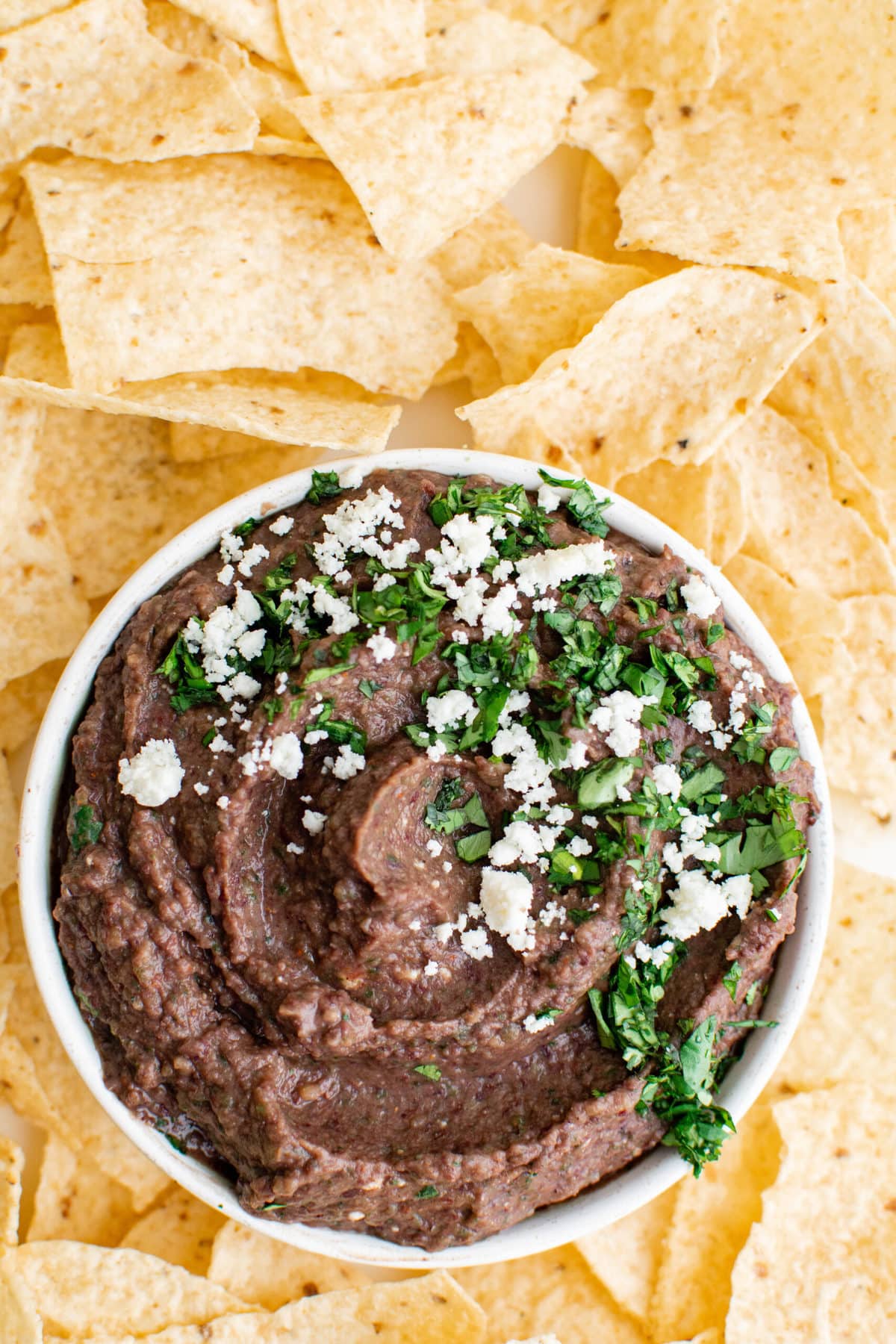 Tortilla chips, black bean dip with cotija cheese and cilantro garnish in a white bowl