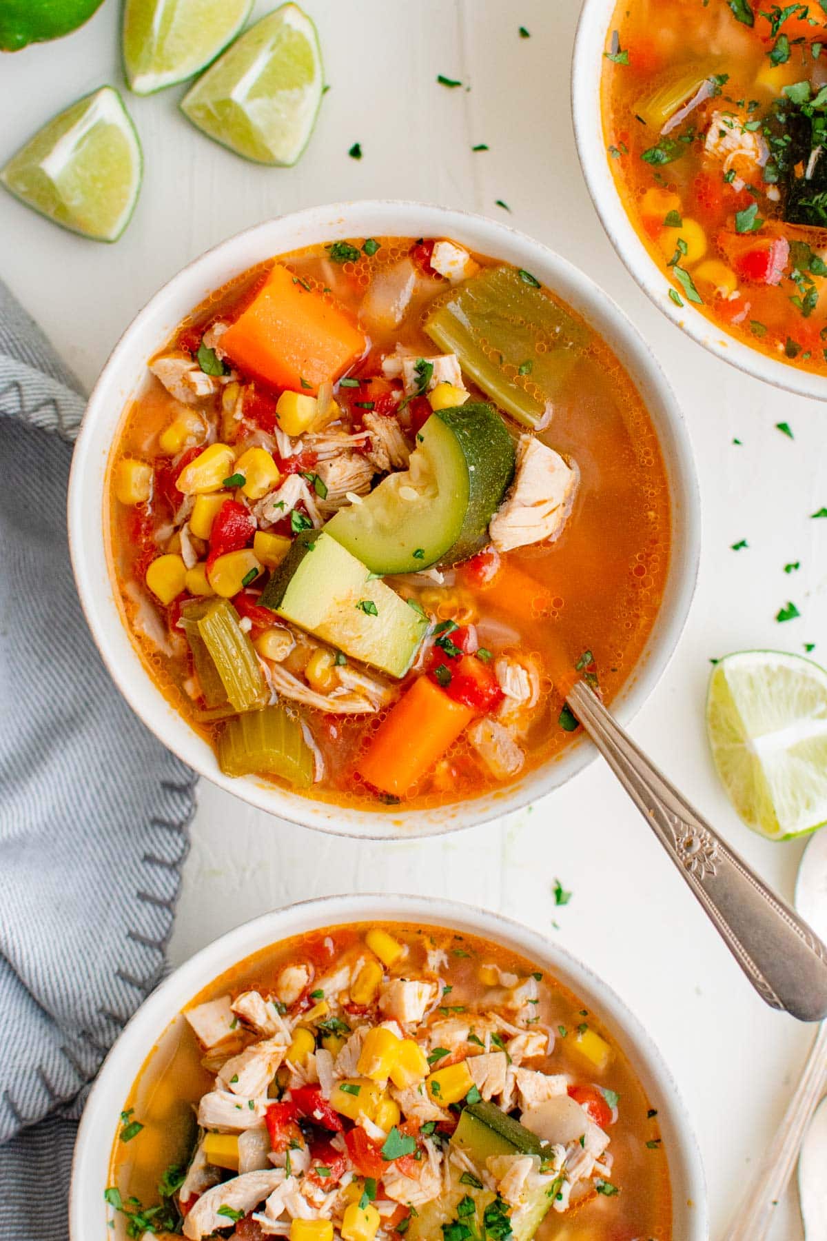 three bowls of chicken soup with zucchini, limes, blue napkin