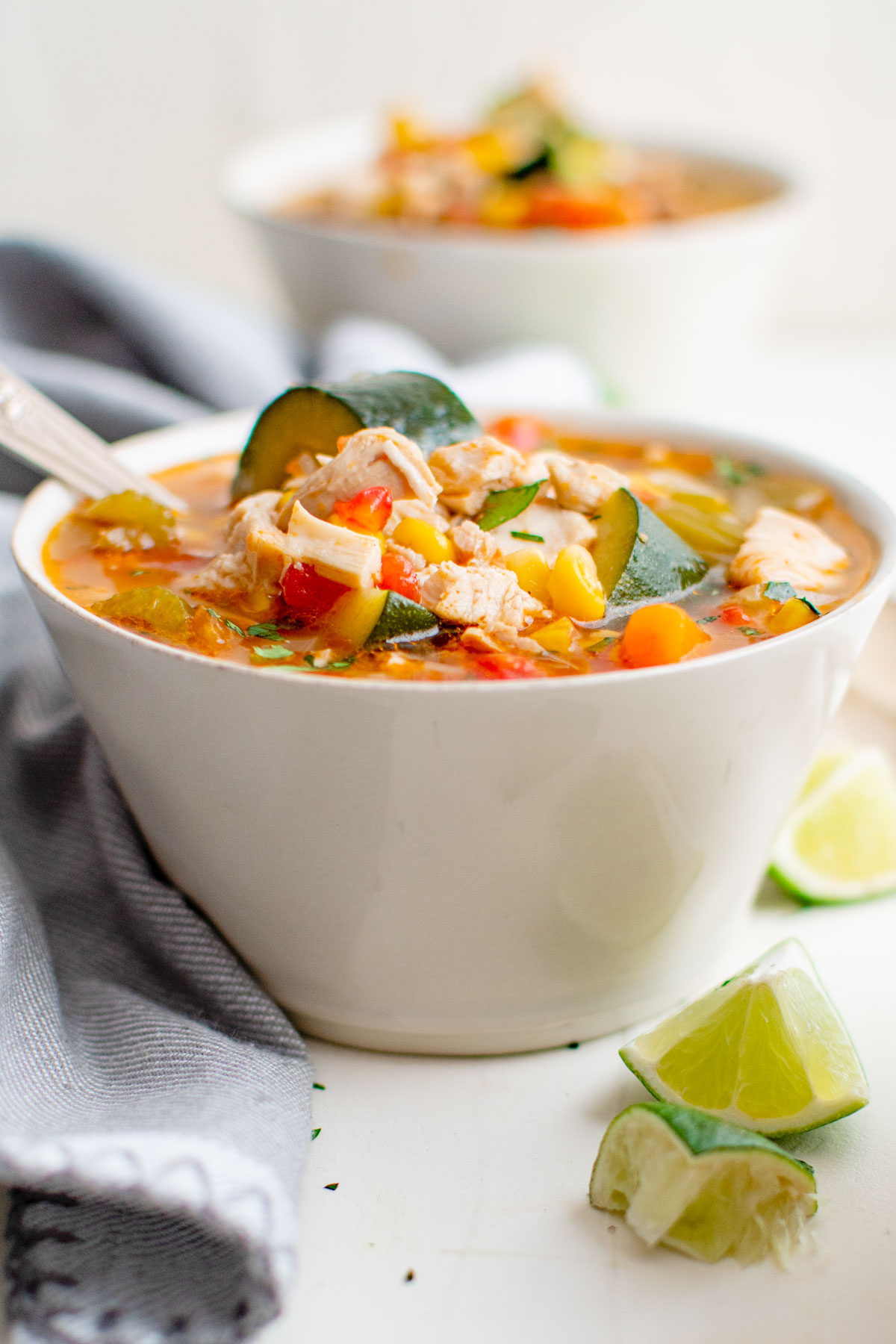 white bowl with caldo de pollo soup, limes, blue napkin