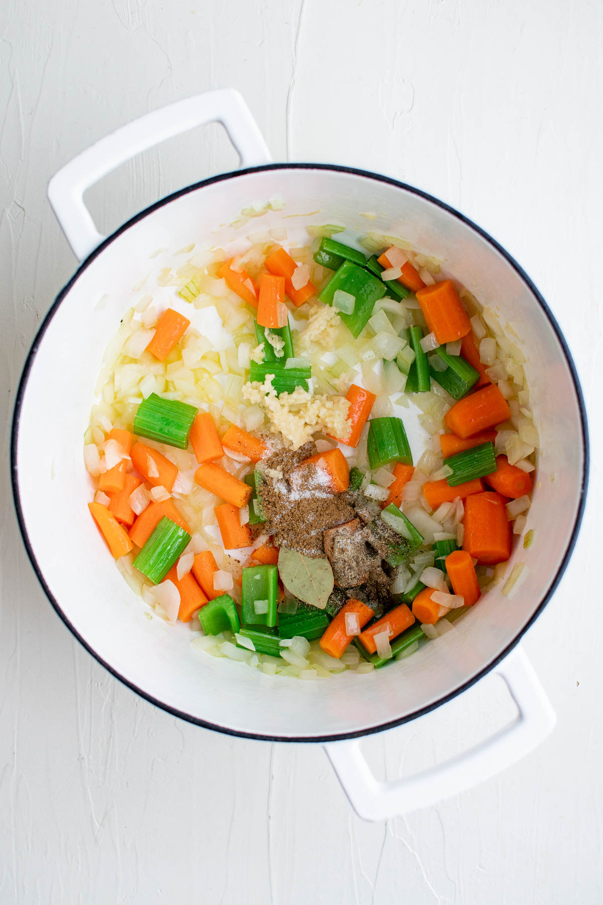 white dutch oven with carrots, celery, onions, bay leave and other spices