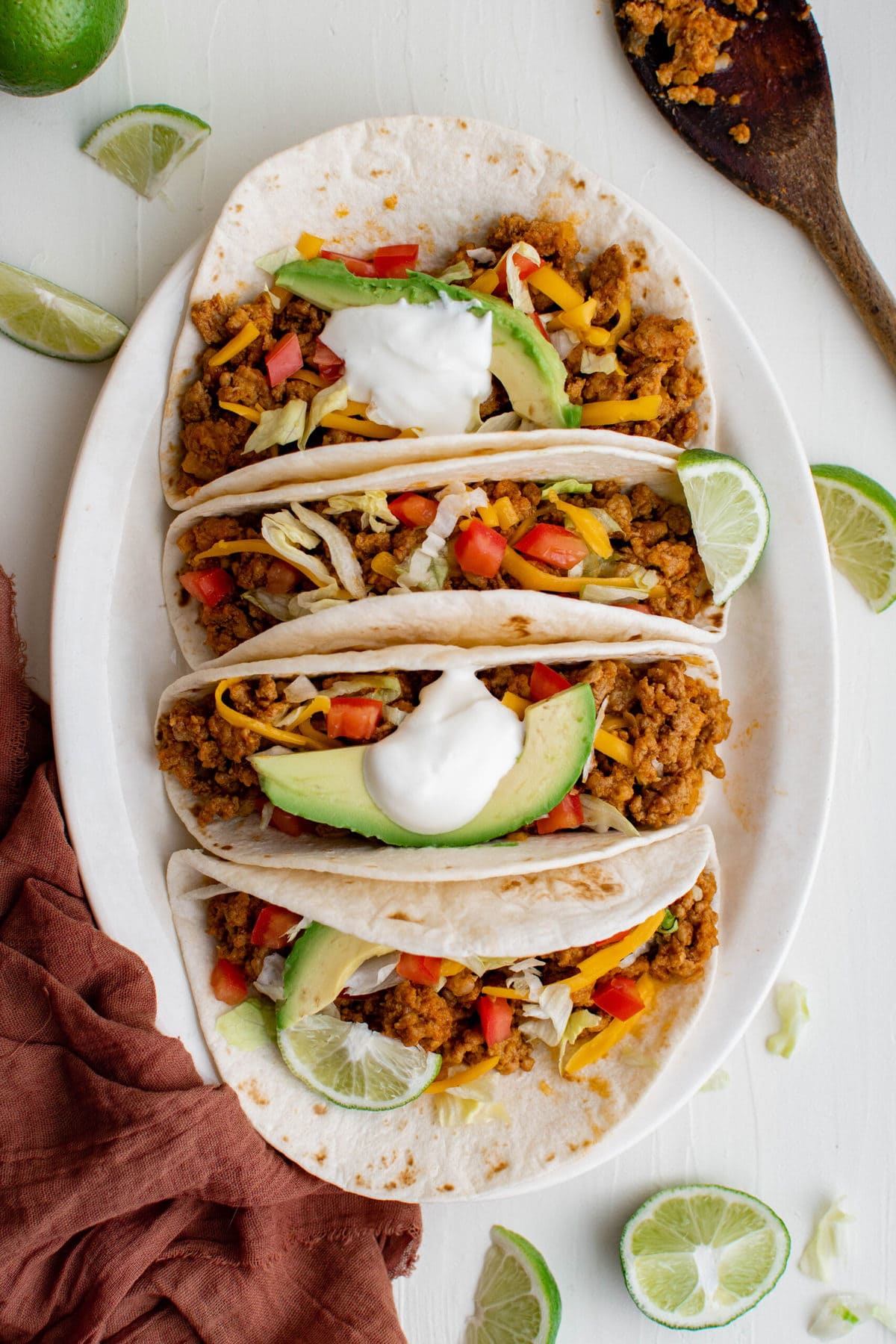 turkey tacos on a white plate, with cheese, lettuce, avocado, sour cream, tomatoes