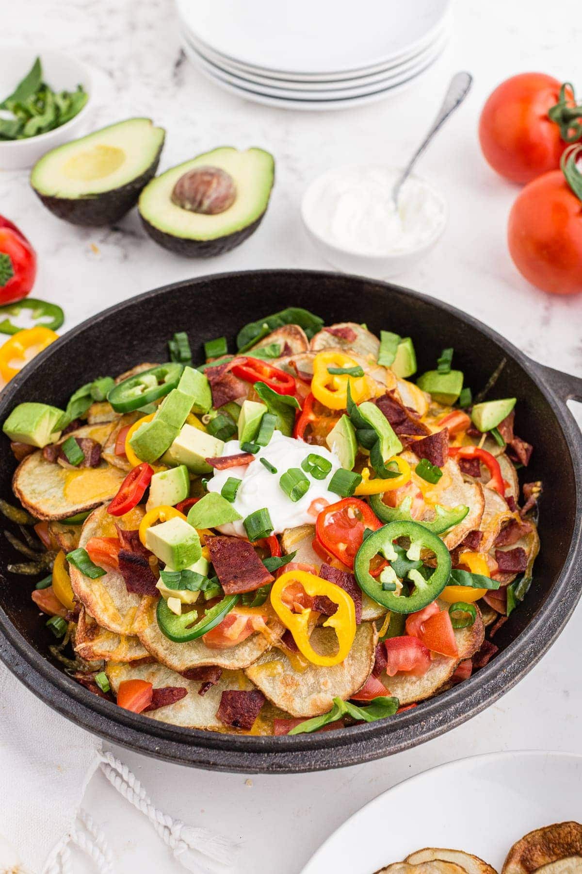 Irish nachos with turkey bacon, melted cheese, green onions, and bell peppers on a black plate.