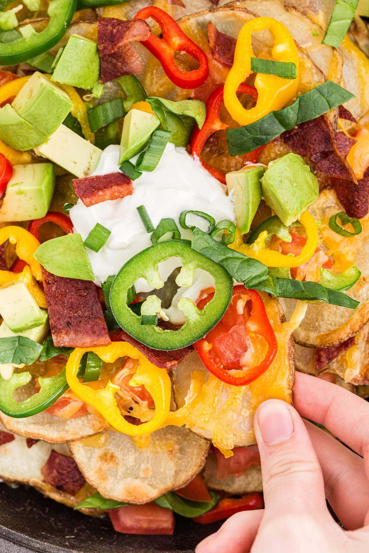 Baked Irish nachos with bell peppers, jalapenos, tomatoes, bacon, and sour cream on baked potato chips.