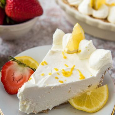 A slice of lemon cheesecake on a white plate with strawberries and lemon on the side