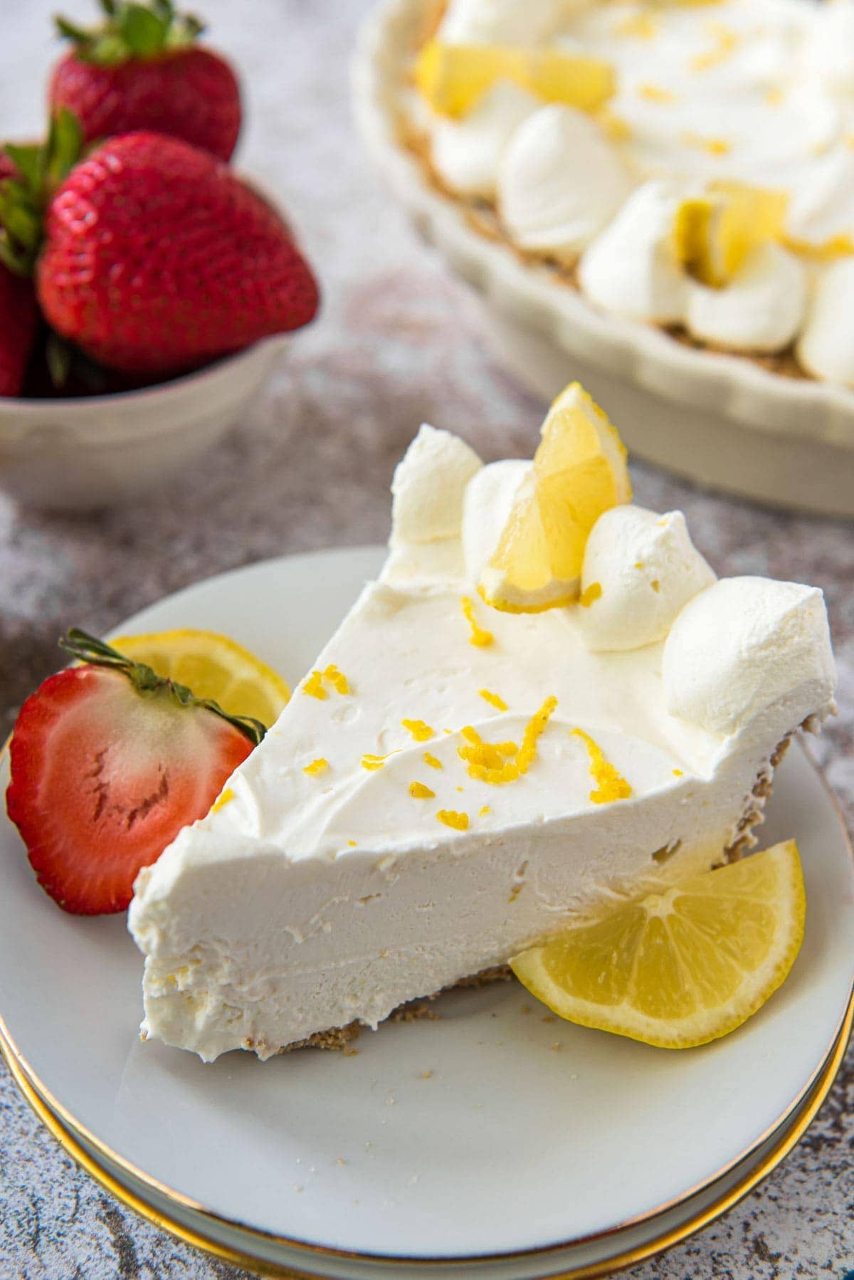 A slice of lemon cheesecake on a white plate with strawberries and lemon on the side