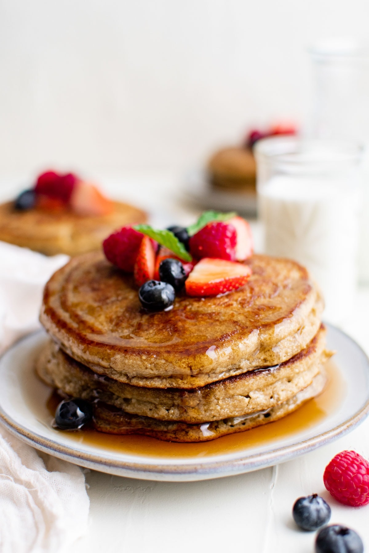 stack of 3 pancakes on a white plate with syrup and fresh berries