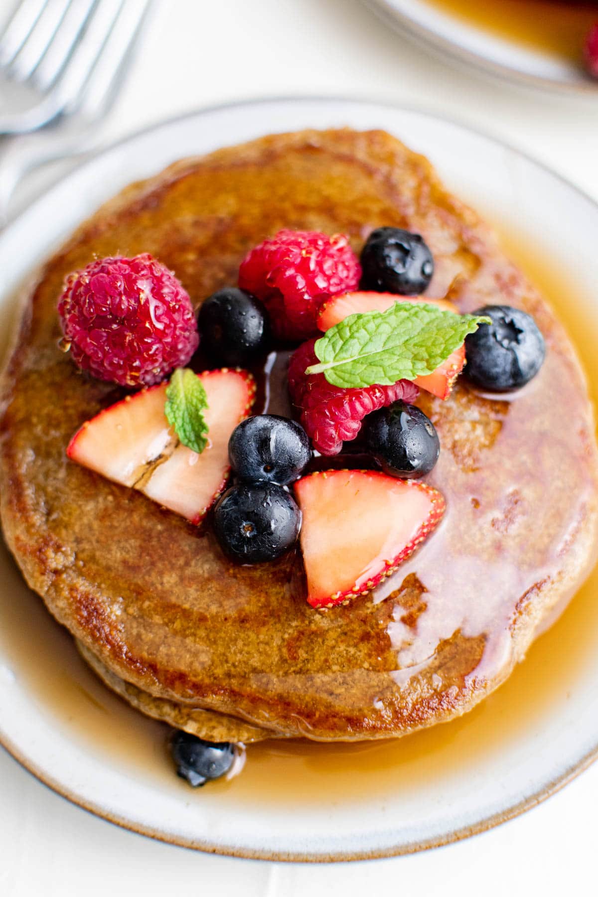 overhead image of oatmeal pancakes on a white plate with syrup and fresh berries