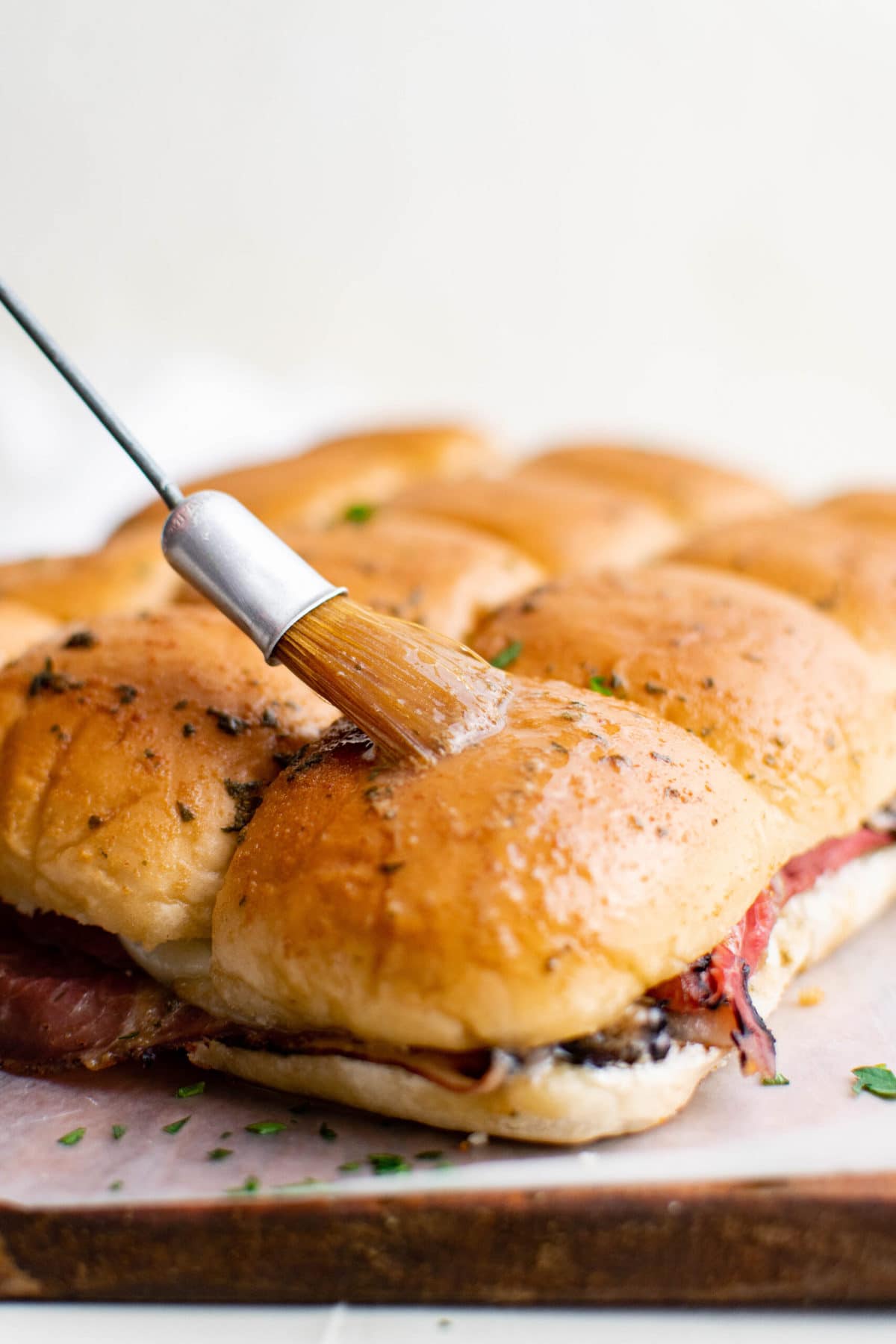 sliders with roast beef, pastry brush brushing butter sauce over the rolls